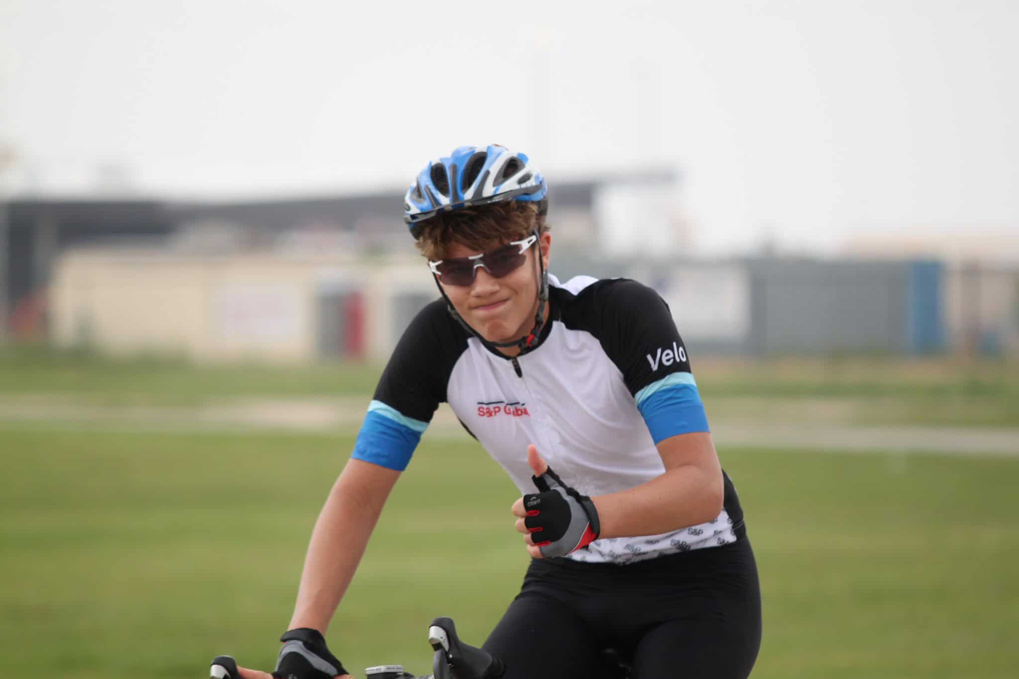 Bright-eyed cyclist in blue and white gear, riding through open green fields on a sunny day.