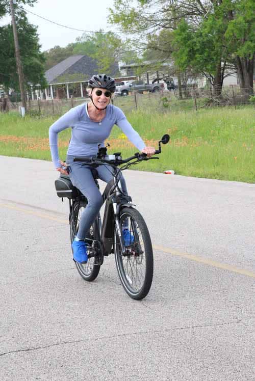 Comfortable woman riding Bluebonnet Express electric bike on suburban road, enjoying eco-friendly cycling.