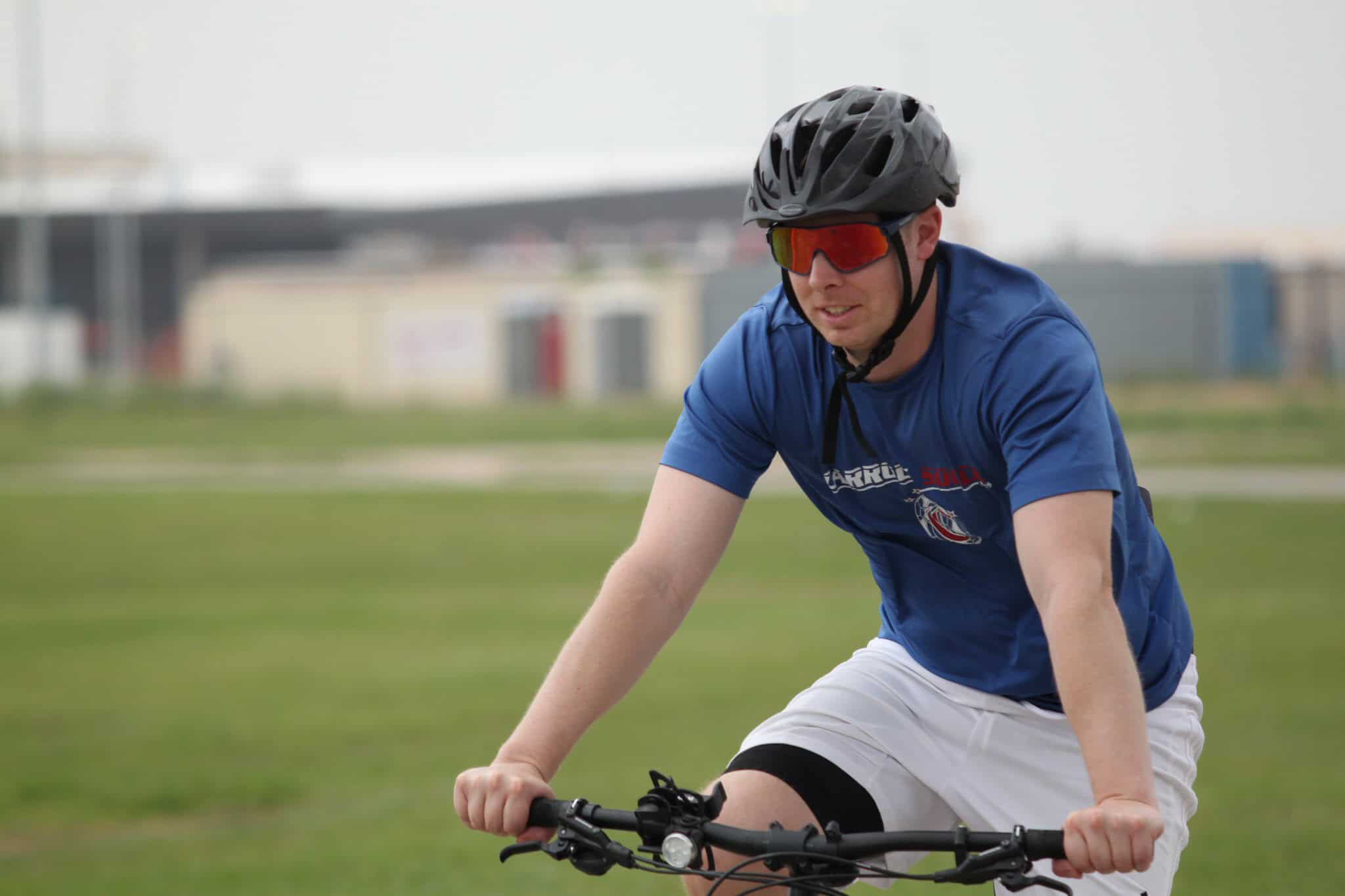 Bicycle rider wearing helmet and sunglasses, actively riding on green field.