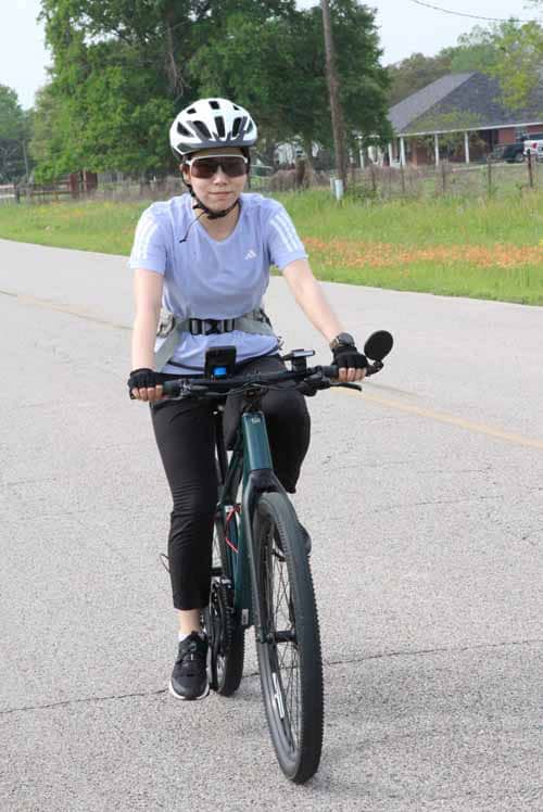 Efficient woman riding a Bluebonnet Express e-bike on a scenic rural road for eco-friendly transportation.