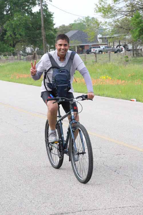 Bright smiling man riding a bicycle on a tree-lined street, enjoying outdoor activity.