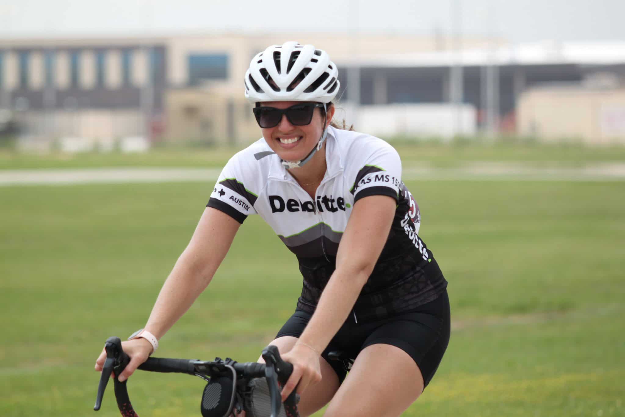 Bike rider smiling during a cycling event, wearing a helmet and sunglasses.