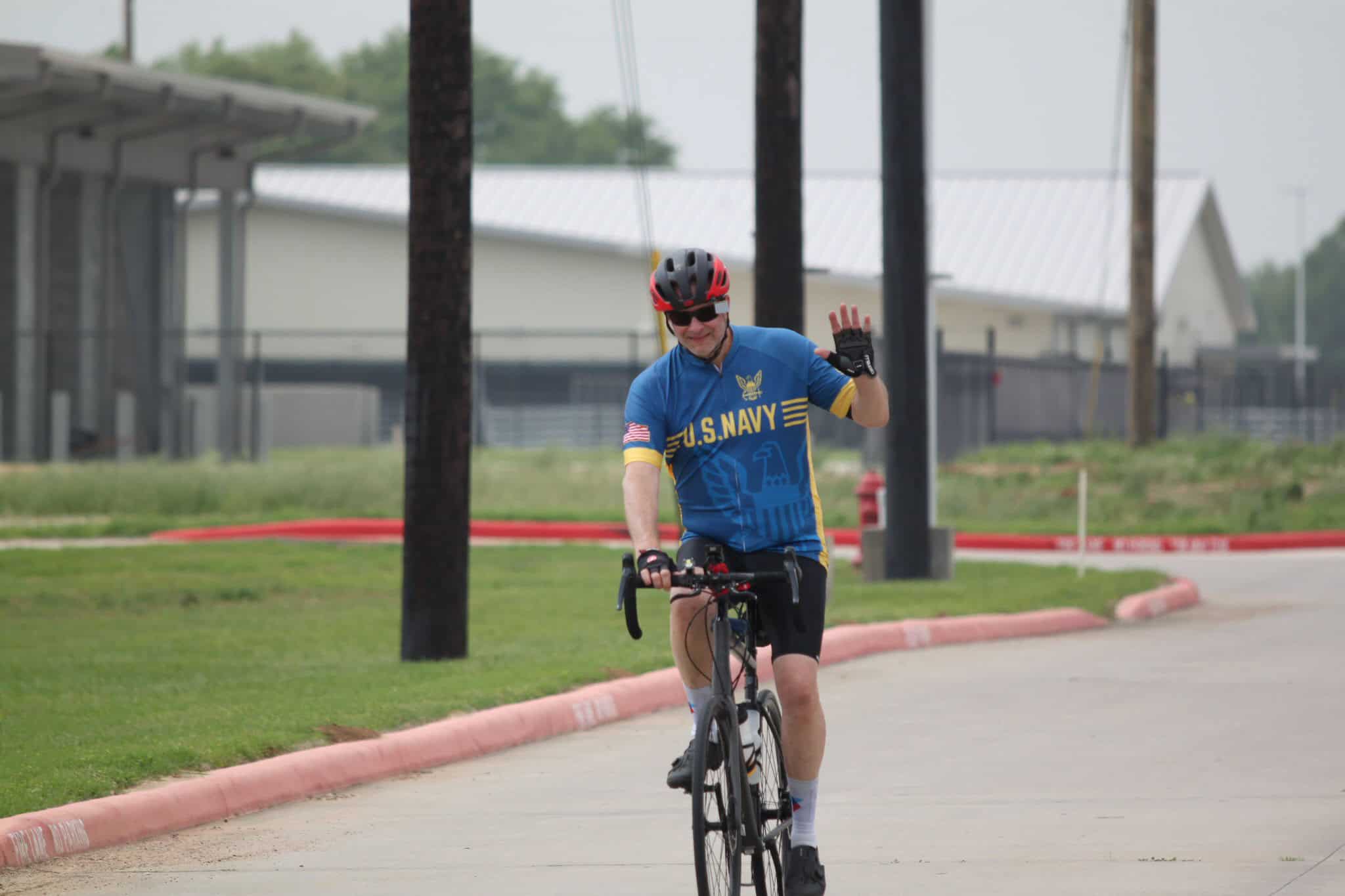 U.S. Navy cyclist waving, riding bike at Bluebonnet Express event, outdoor recreational cycling activity.