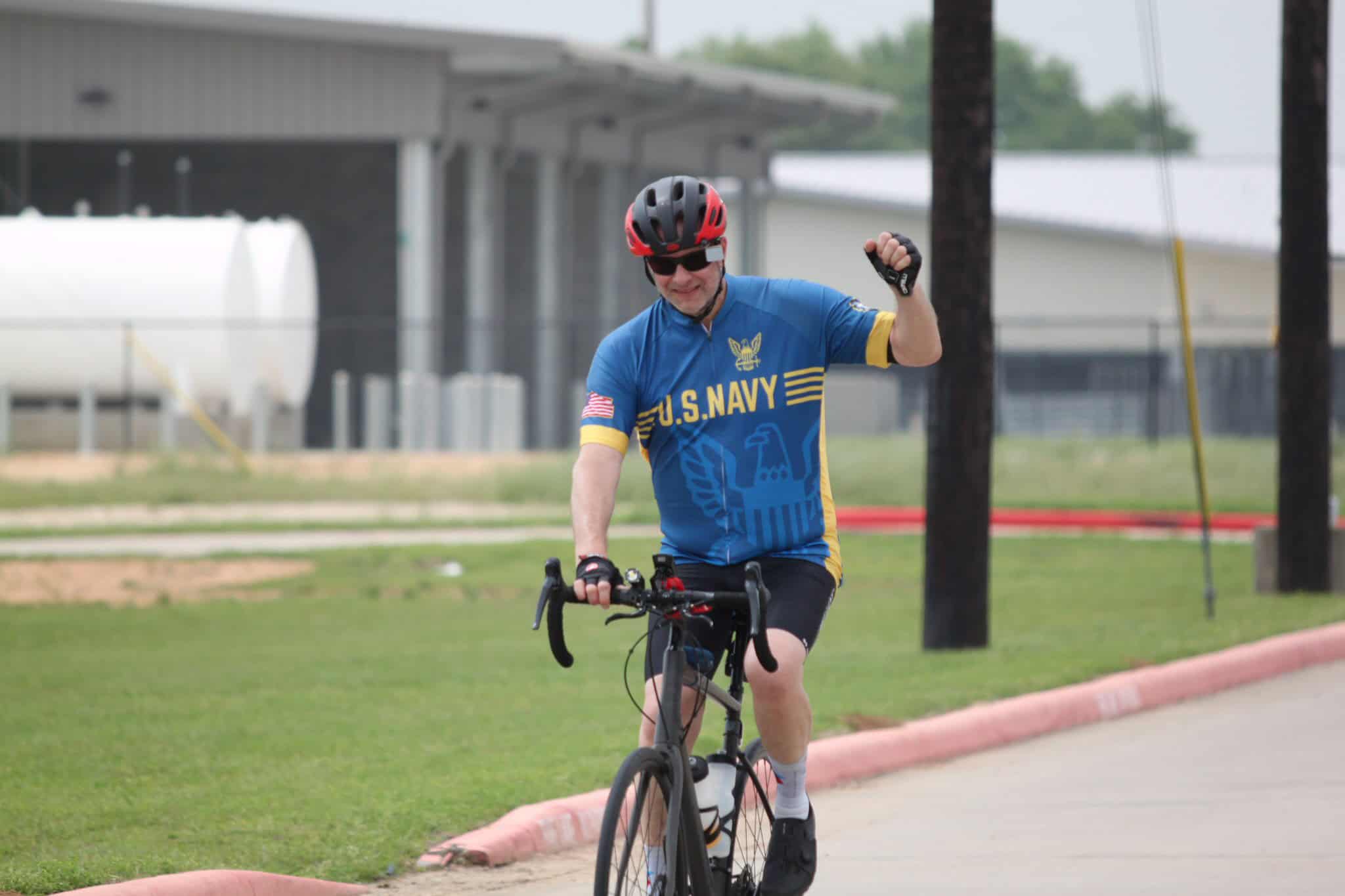 Bright blue U.S. Navy cycling jersey, helmet, sunglasses, and gloves on a happy cyclist riding outdoors.