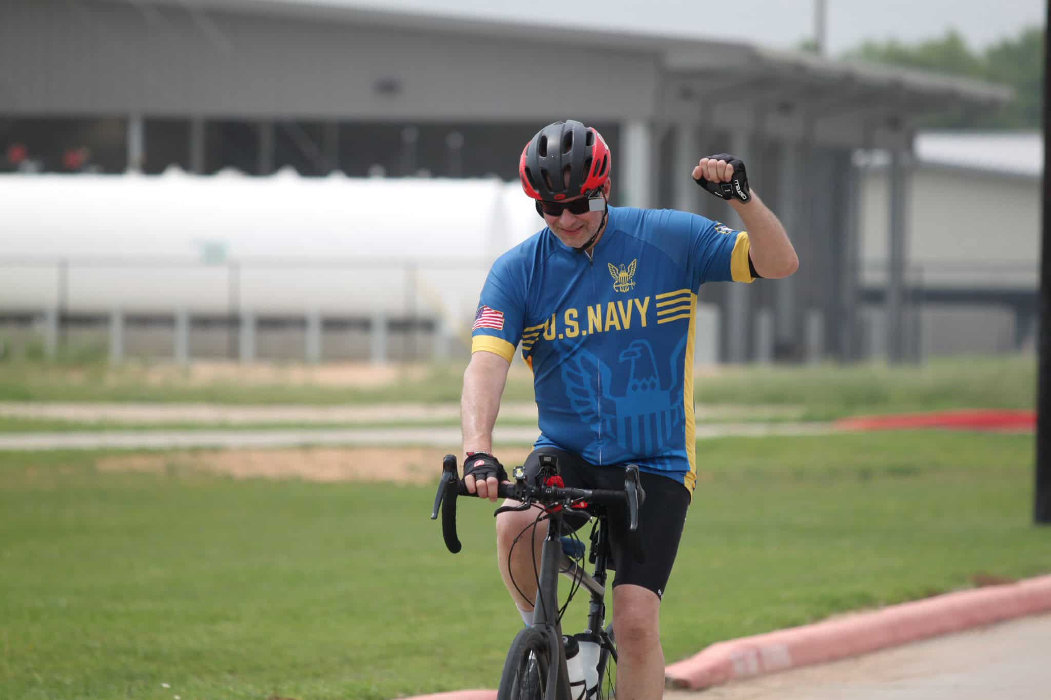 Vibrant Bluebonnet Express cyclist wearing U.S. Navy jersey, riding bike with enthusiasm outdoors.
