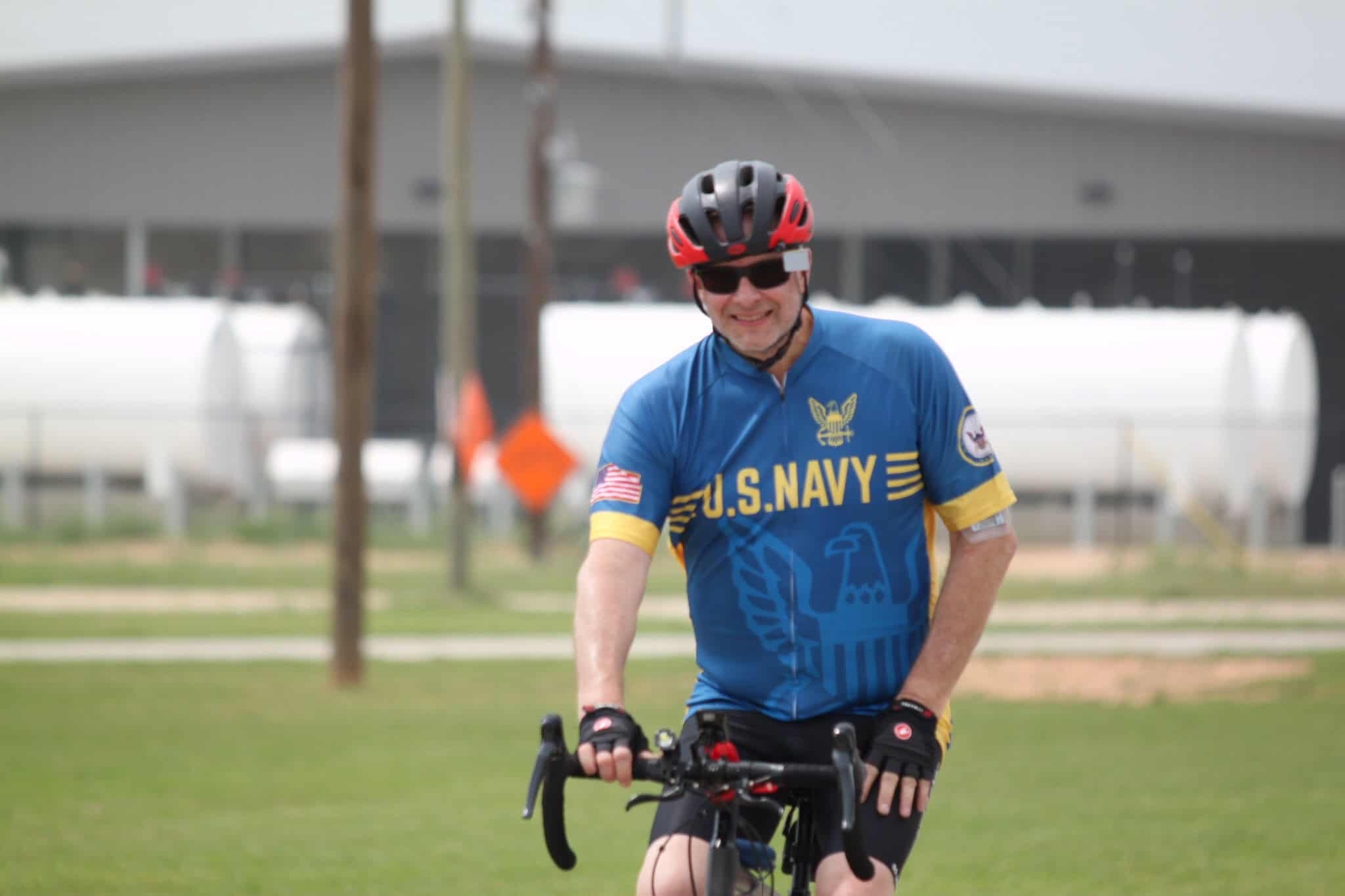 Vibrant cyclist wearing U.S. Navy jersey riding a bike outdoors, promoting Bluebonnet Express.