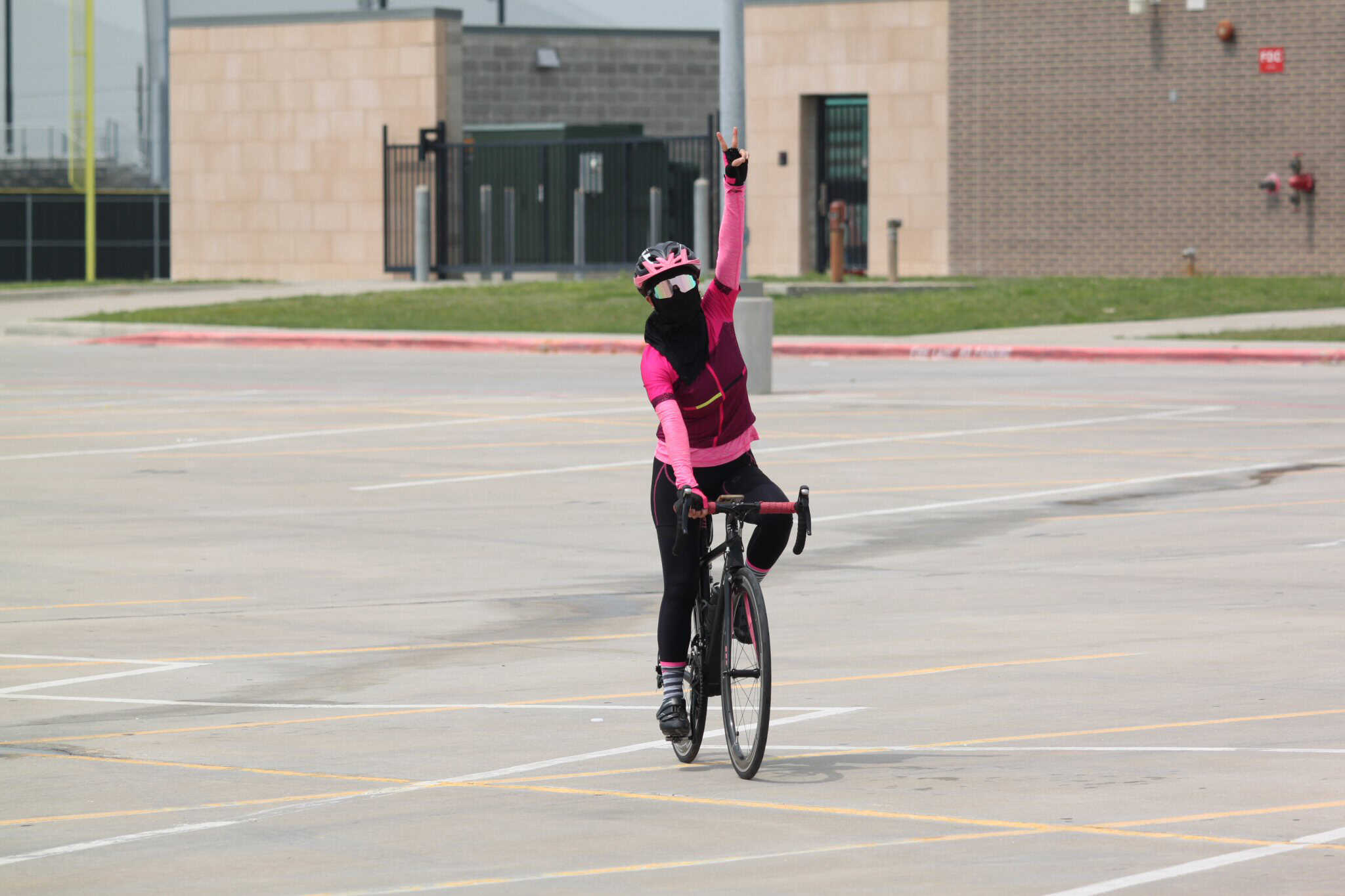 Pink cyclist making peace sign in empty parking lot for Bluebonnet Express promotional shot.