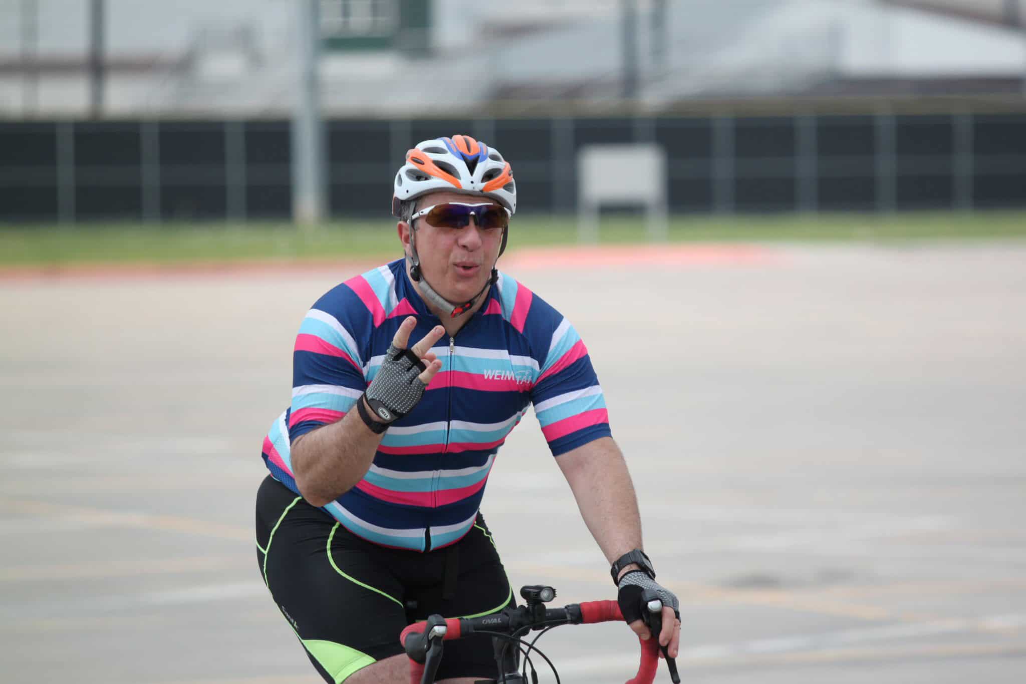 Male cyclist wearing a colorful jersey and helmet riding bike outdoors during daytime.