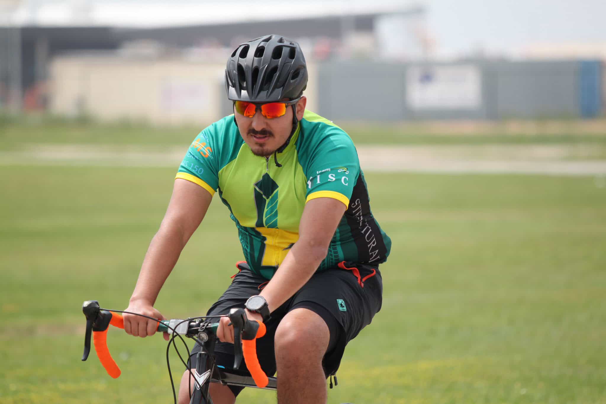 High-energy cyclist wearing helmet and sunglasses riding on grassy field, promoting Bluebonnet Express bike services.