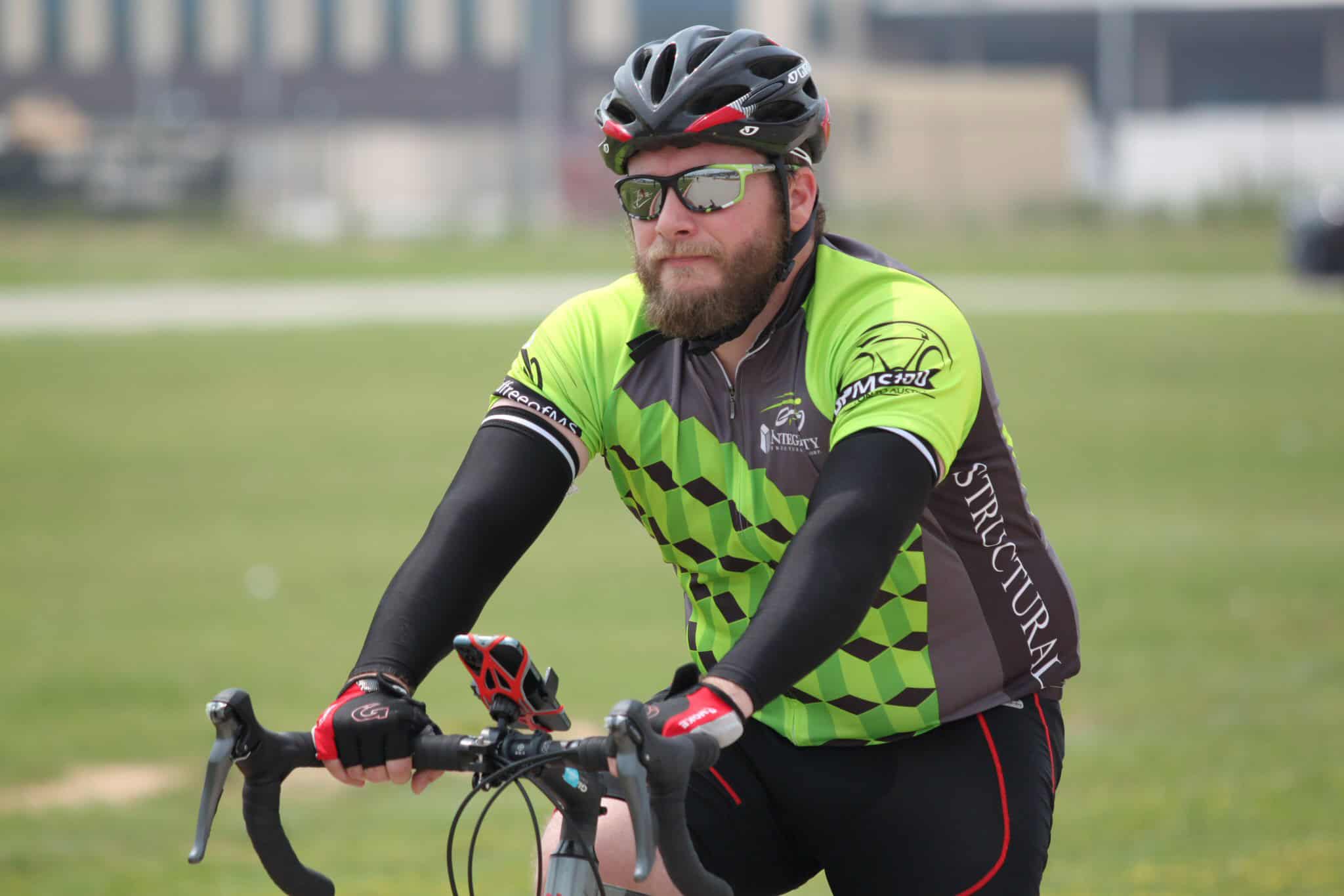 Cyclist riding a green and black bike jersey on outdoor trail during daytime.