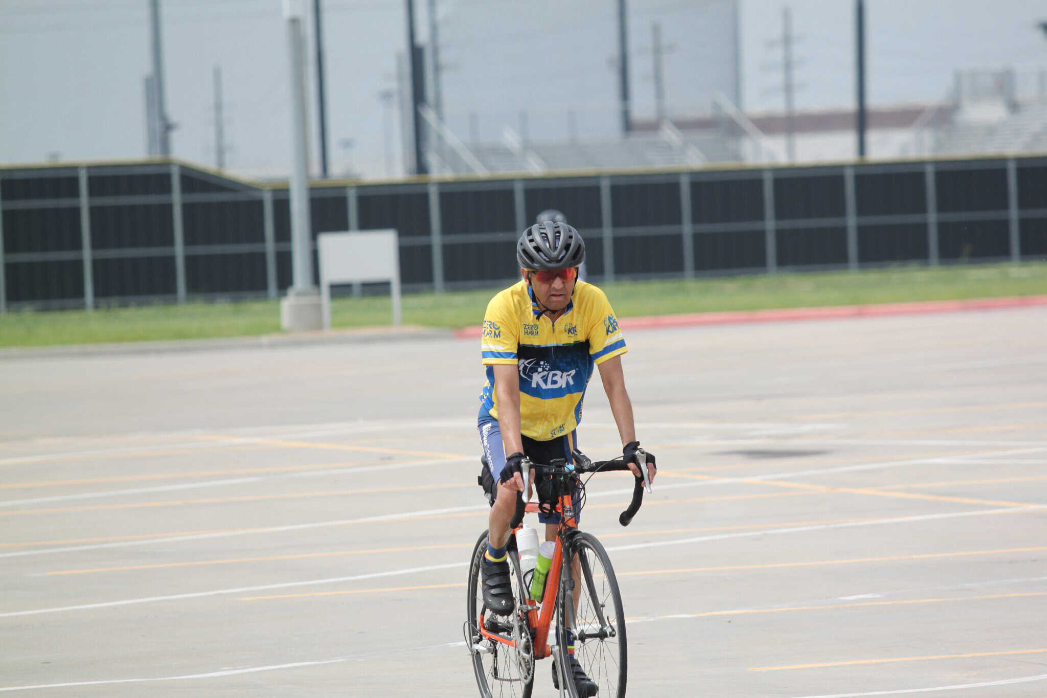 Cyclist riding on a bike lane in an outdoor parking lot with stadium in background.
