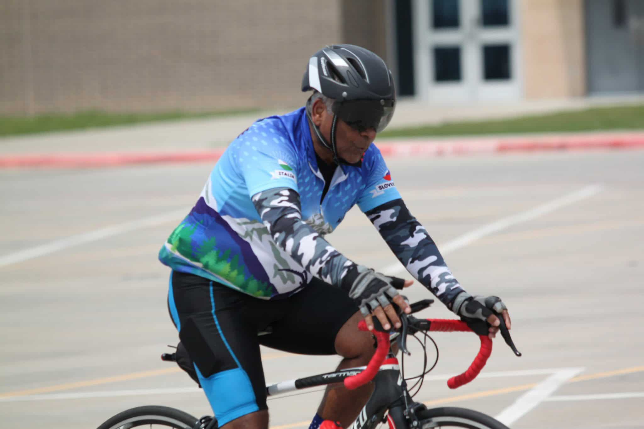 Rider on a road bike wearing a helmet, colorful cycling gear, and gloves in an outdoor setting.
