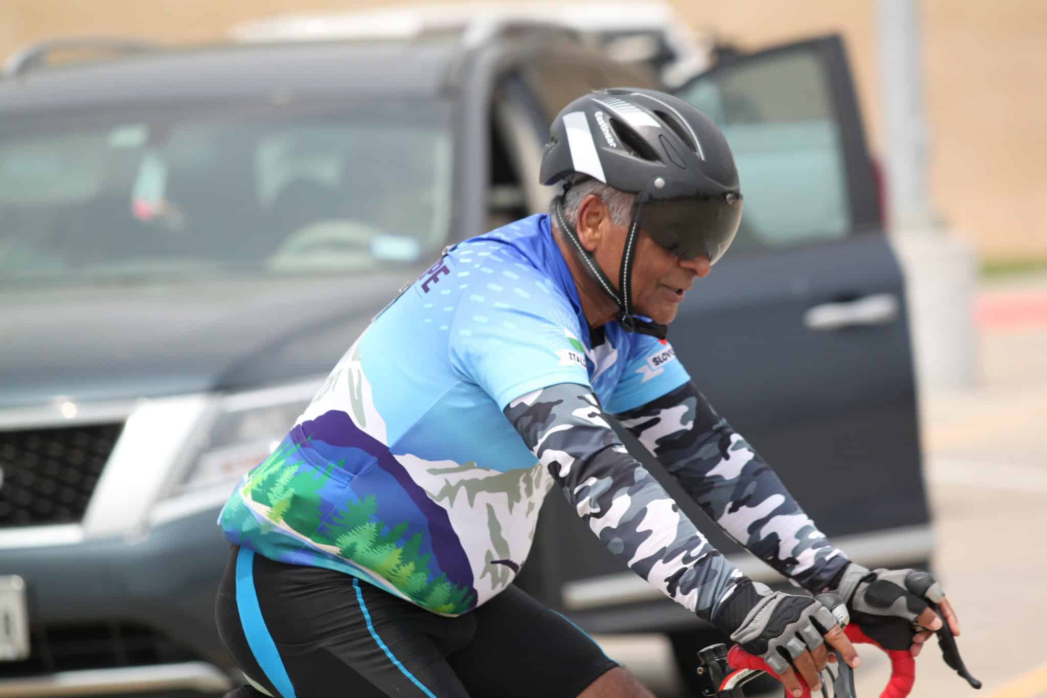 Older man cycling in Bluebonnet Express cycling jersey with helmet and gloves, outdoors.
