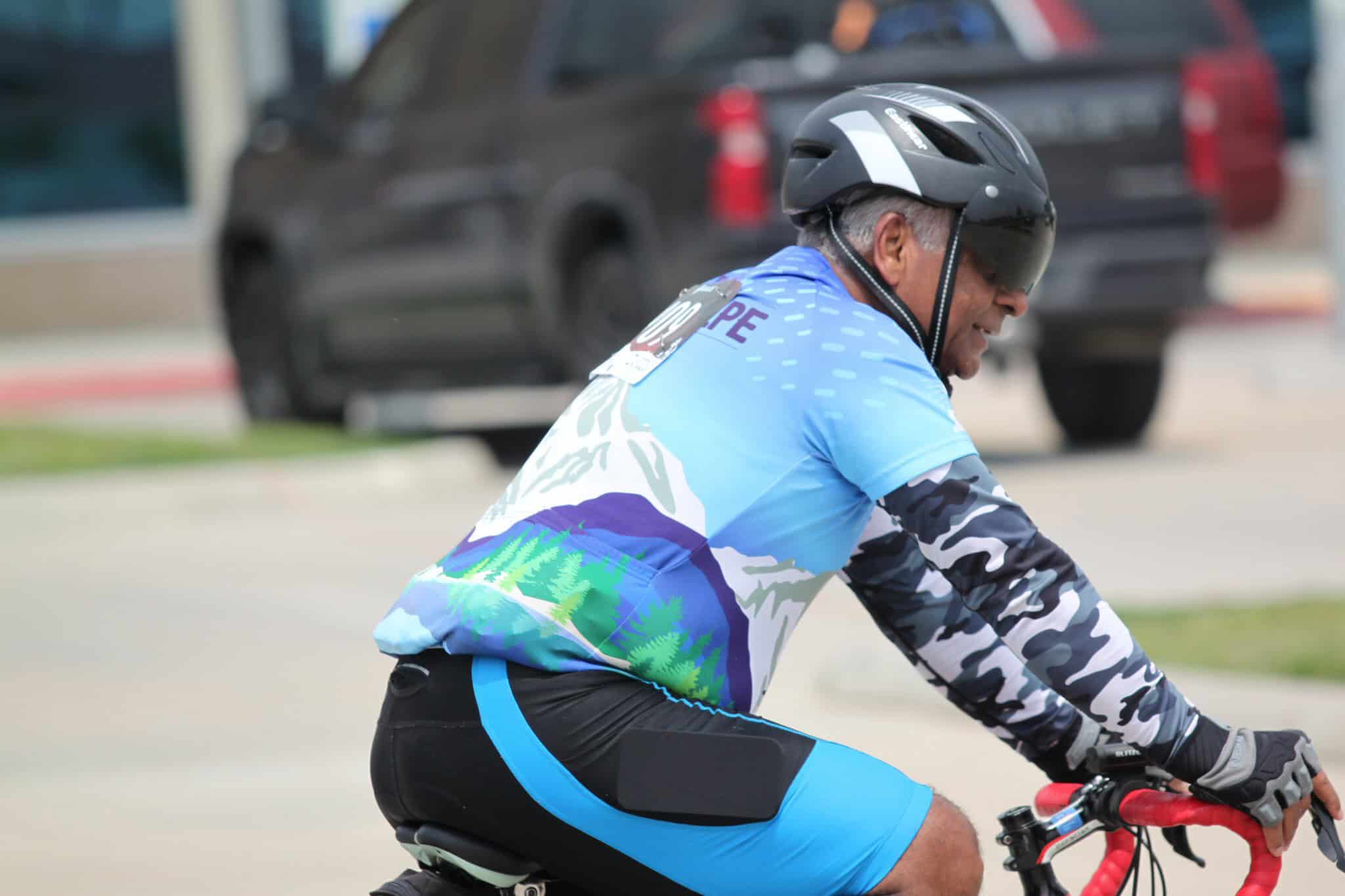 A man riding a bike wearing a Bluebonnet Express cycling jersey and helmet on a city street.