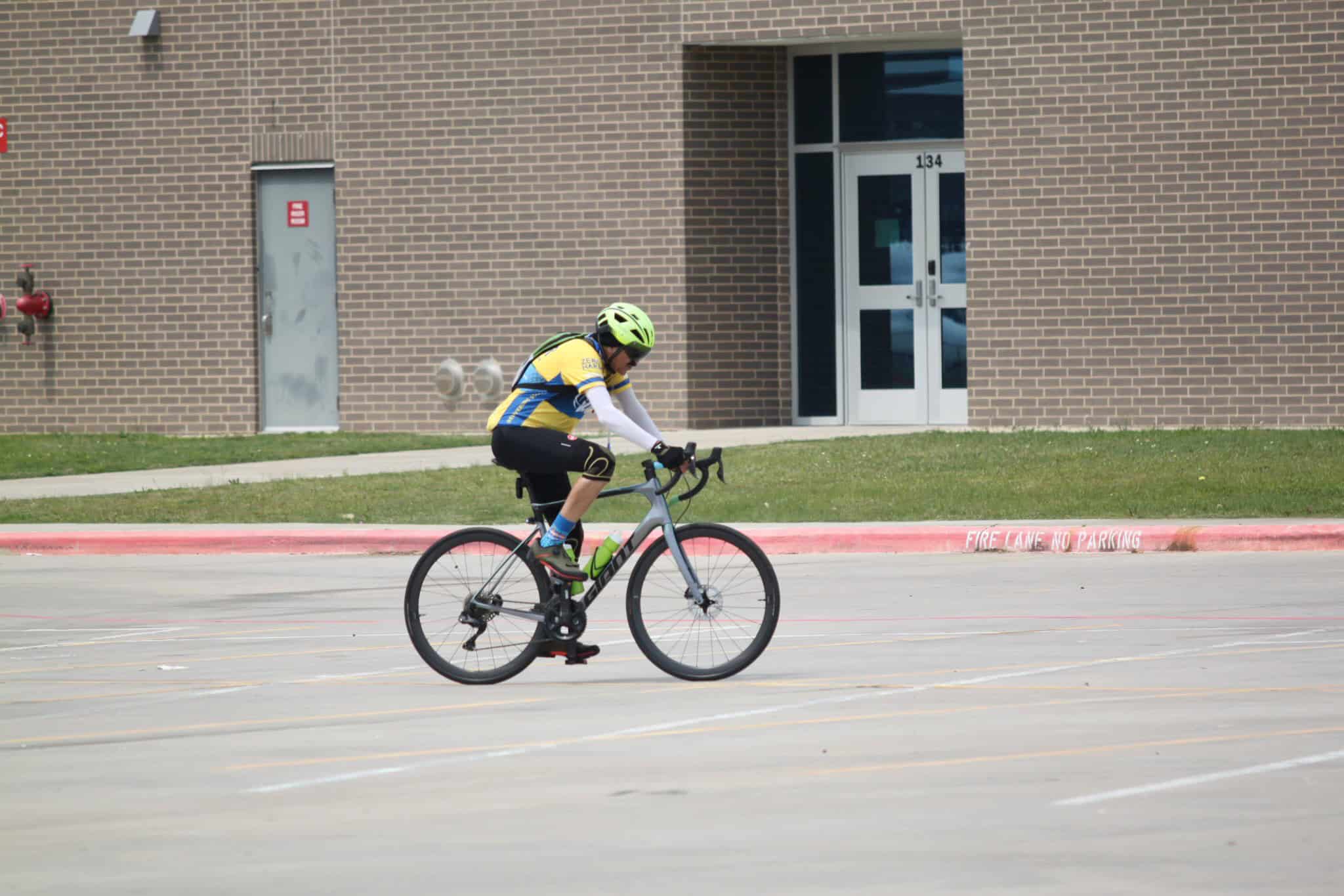 Bright cyclist riding a bike on city street in Bluebonnet Express bike gear, sunny day.