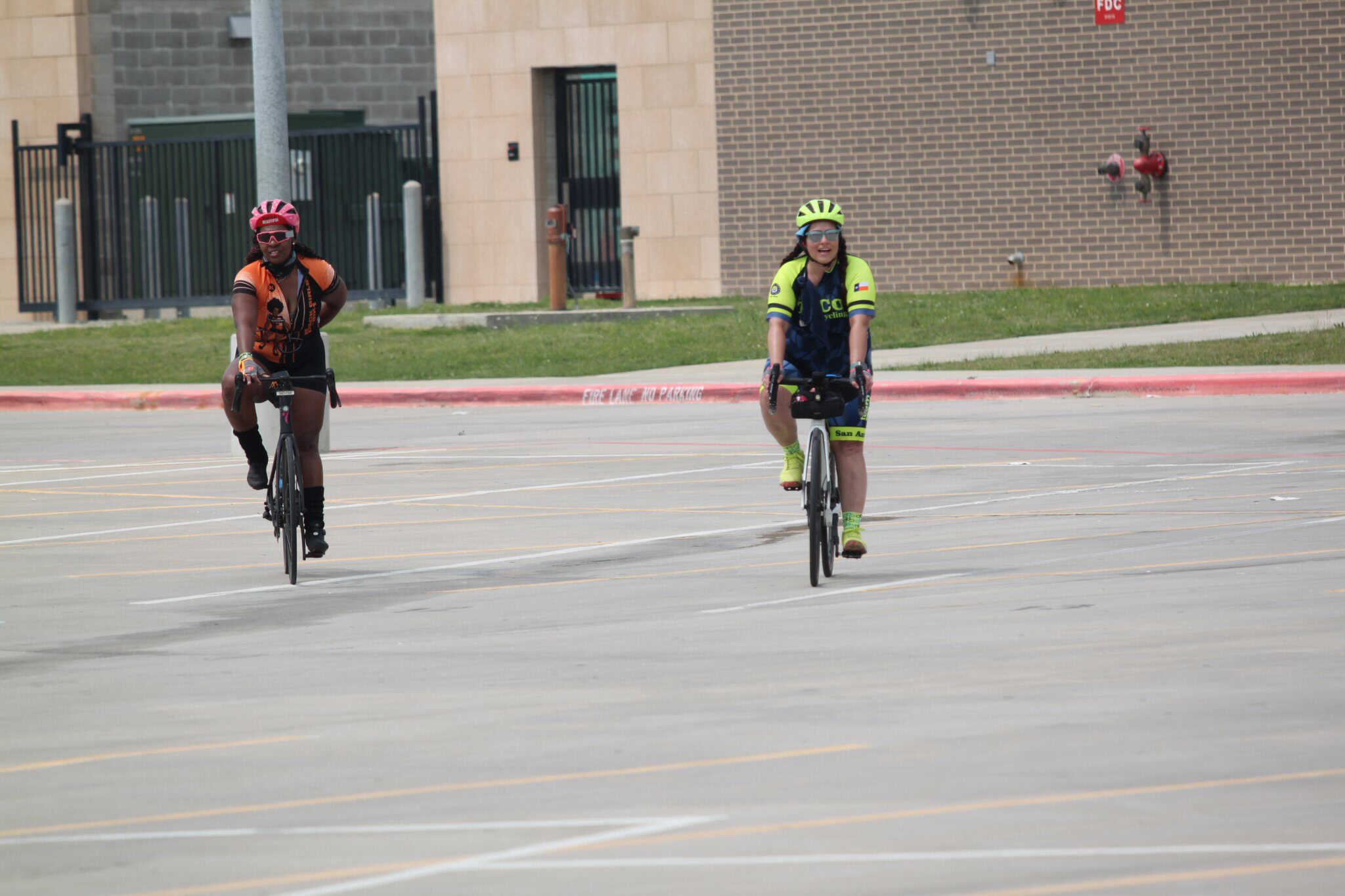 Brightly dressed female cyclists riding bikes in an open parking lot during daytime.