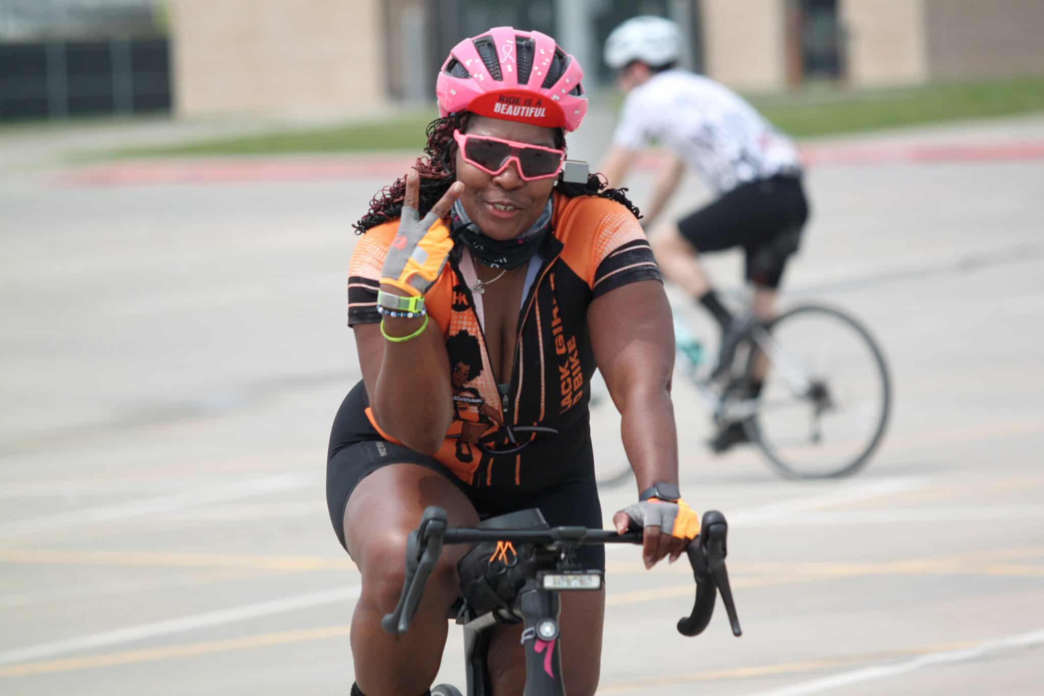 Colorful female cyclist wearing Black Girl Magic jersey, pink helmet, and sunglasses during Bluebonnet Express ride.