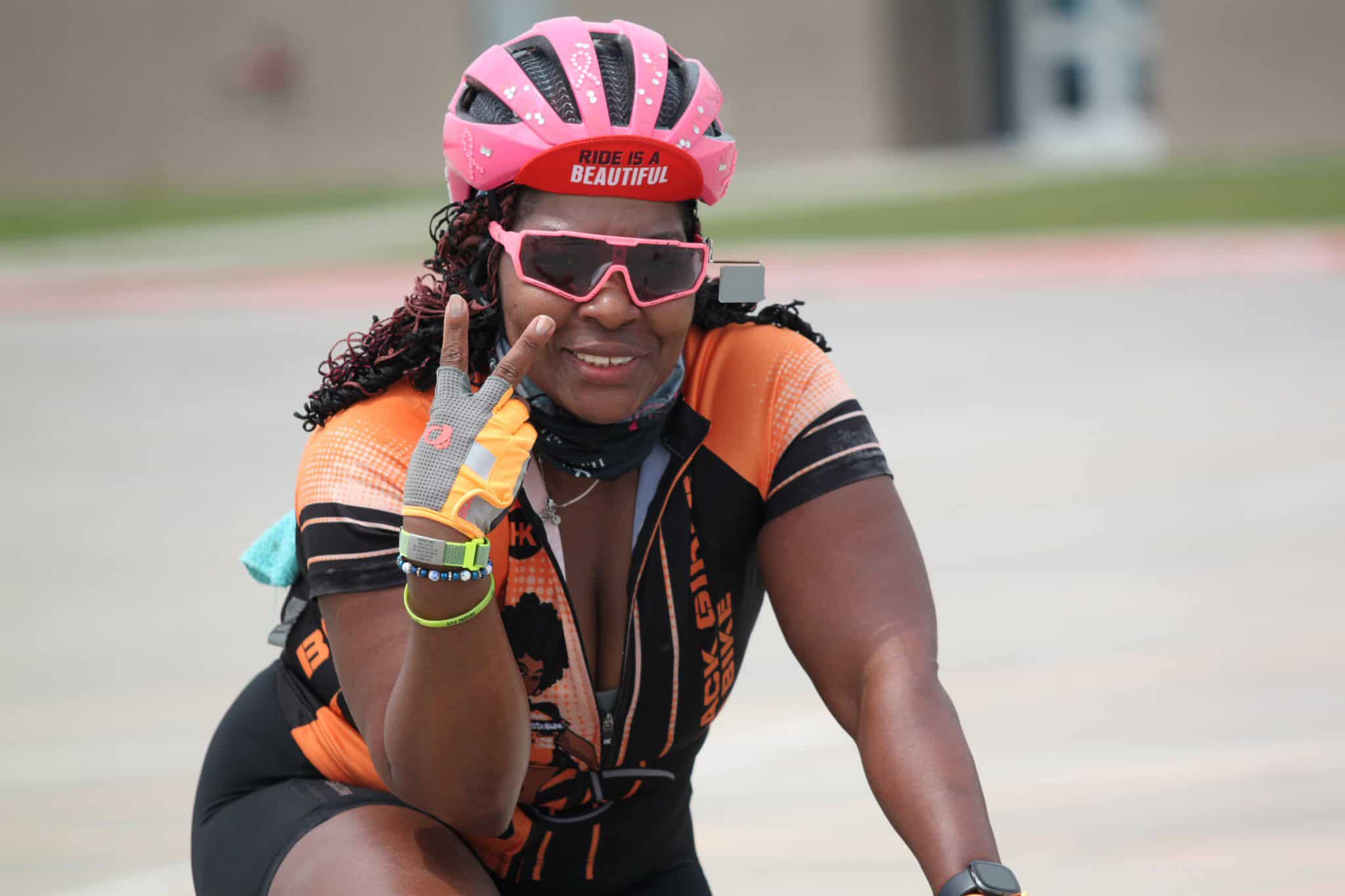 Bright female cyclist wearing pink helmet and sunglasses, smiling and posing outdoors, promoting Bluebonnet Express cycling event.
