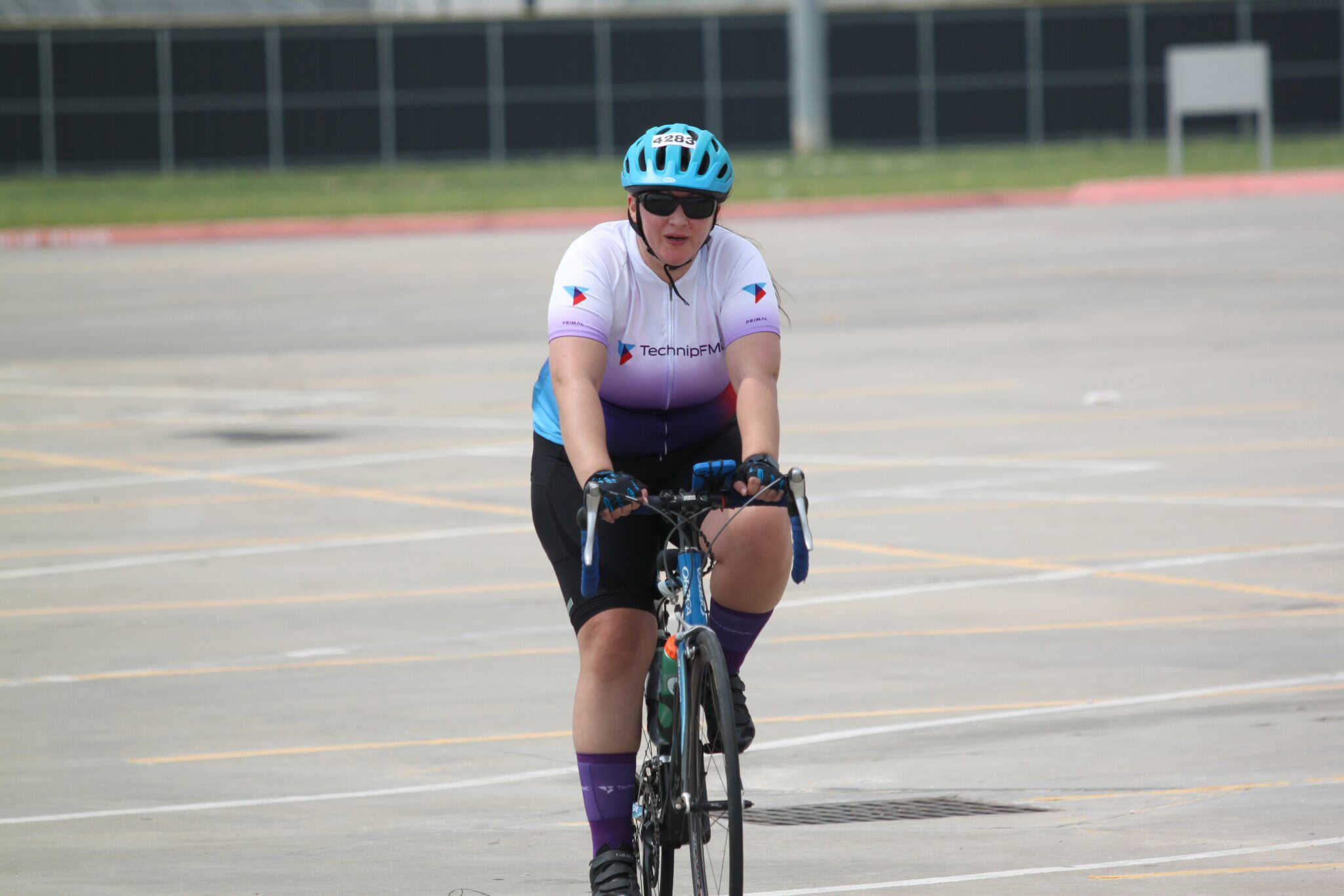 Women cyclist in Bluebonnet Express jersey riding on a parking lot.