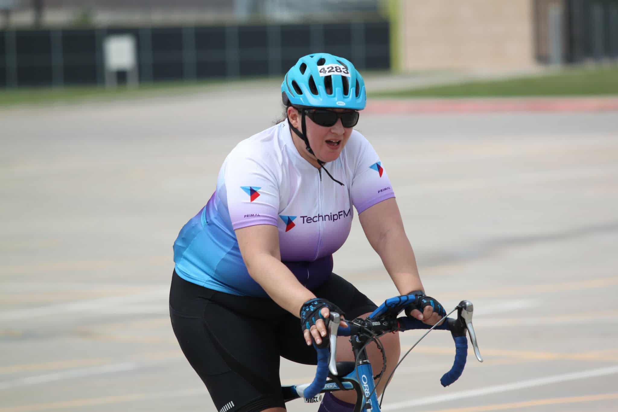 Vegan woman cyclist wearing helmet and sunglasses during Bluebonnet Express race event.
