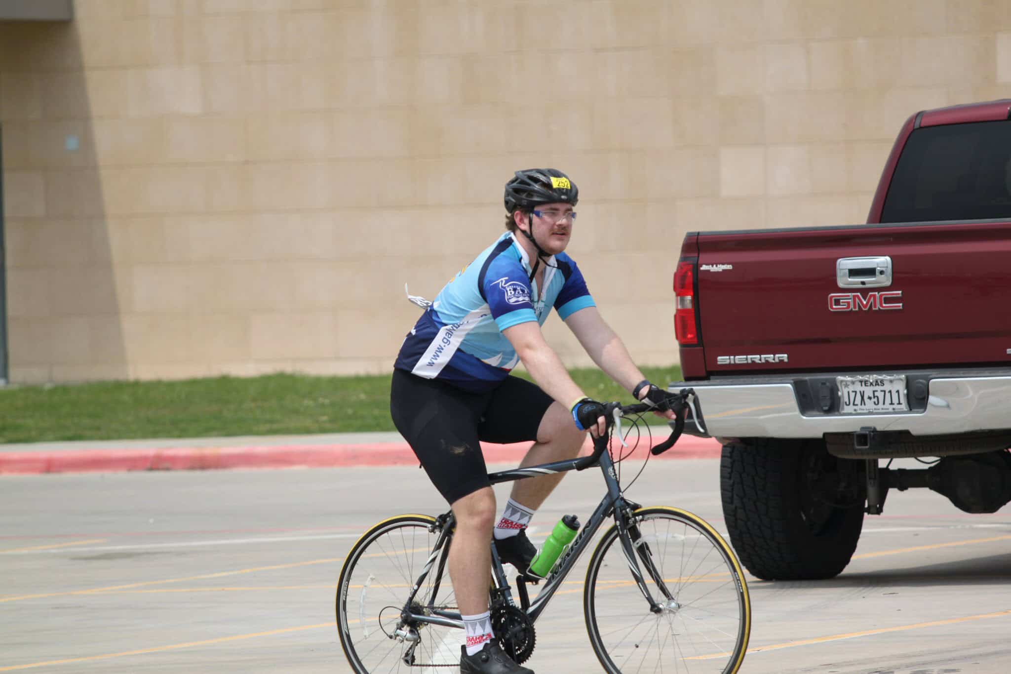 Young male cyclist riding bike near GMC Sierra truck on city street.