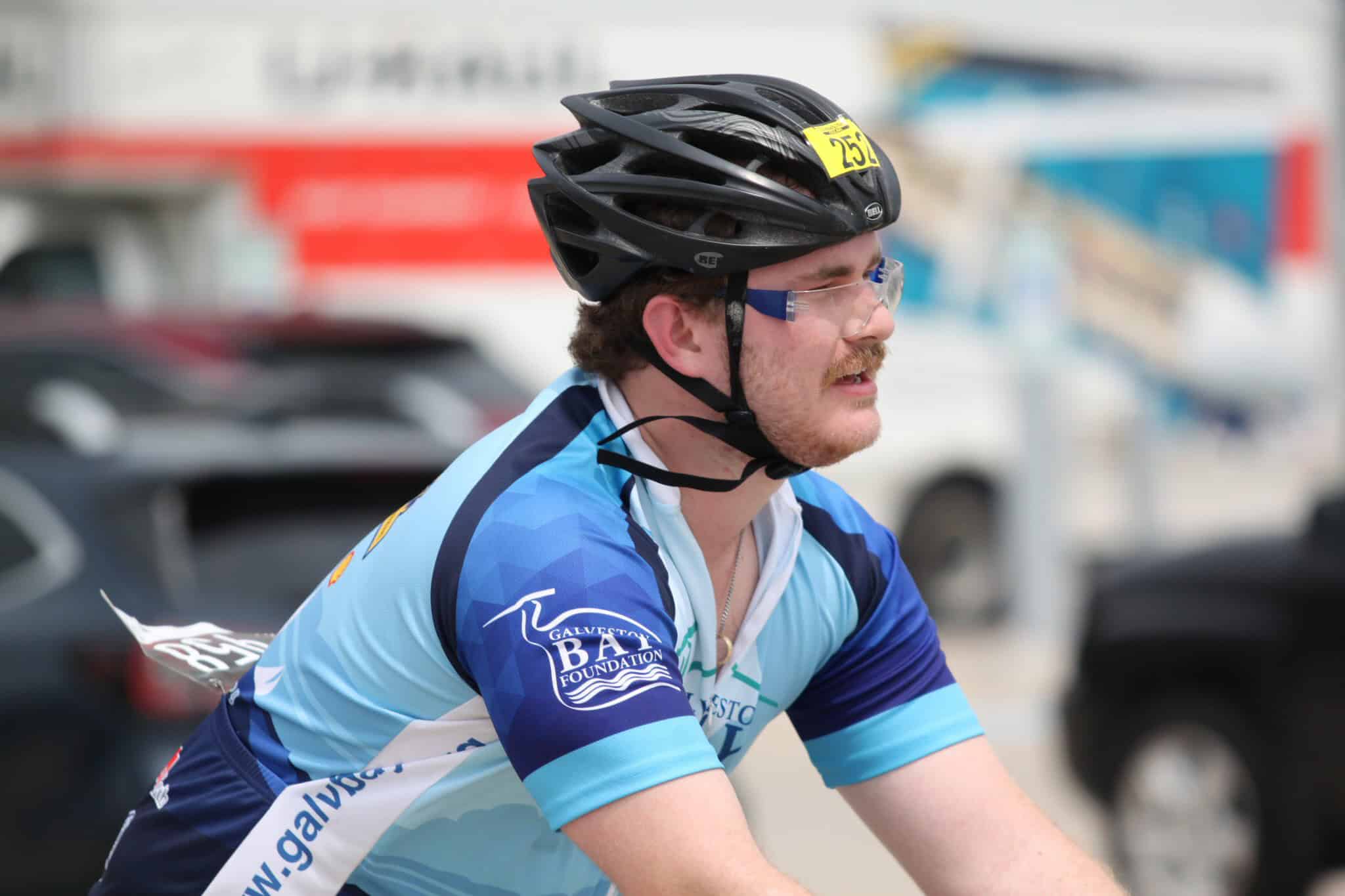 Bike racer wearing a black helmet and blue jersey, participating in a cycling event.