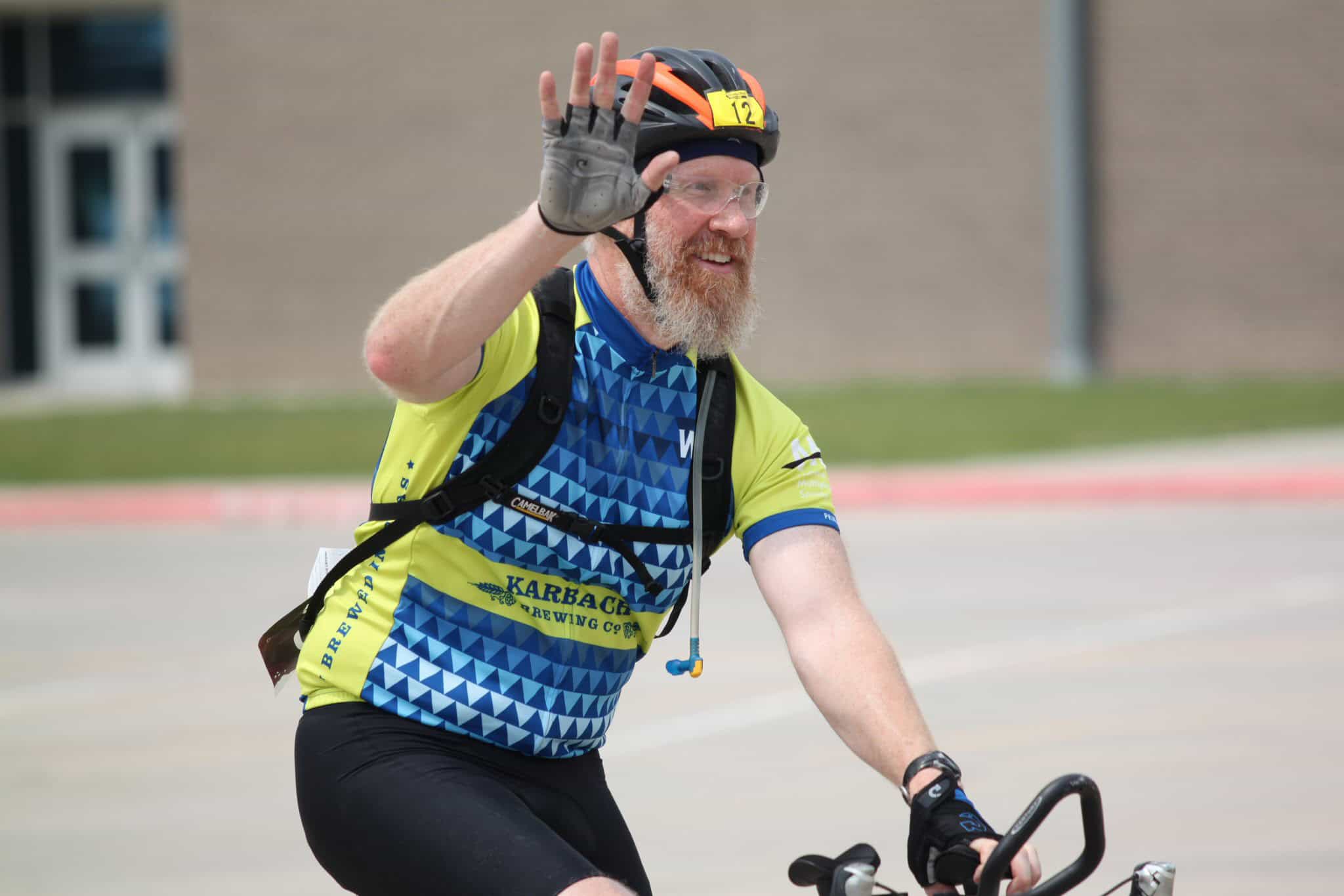 Bright yellow and blue cycling jersey, smiling male cyclist waving during Bluebonnet Express event.