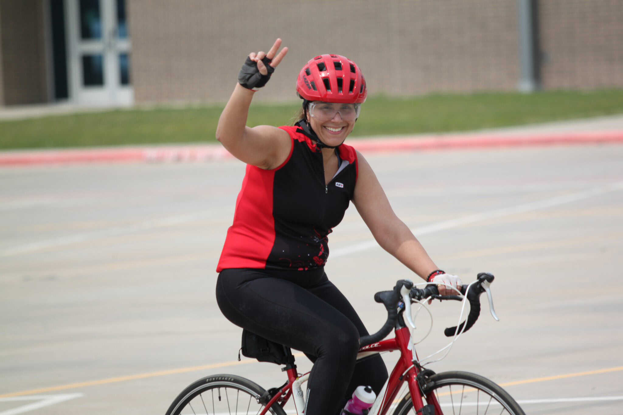 Women cycling race, smiling cyclist in red helmet and sportswear on bike, participating in outdoor event, healthy active lifestyle, Bluebonnet Express.
