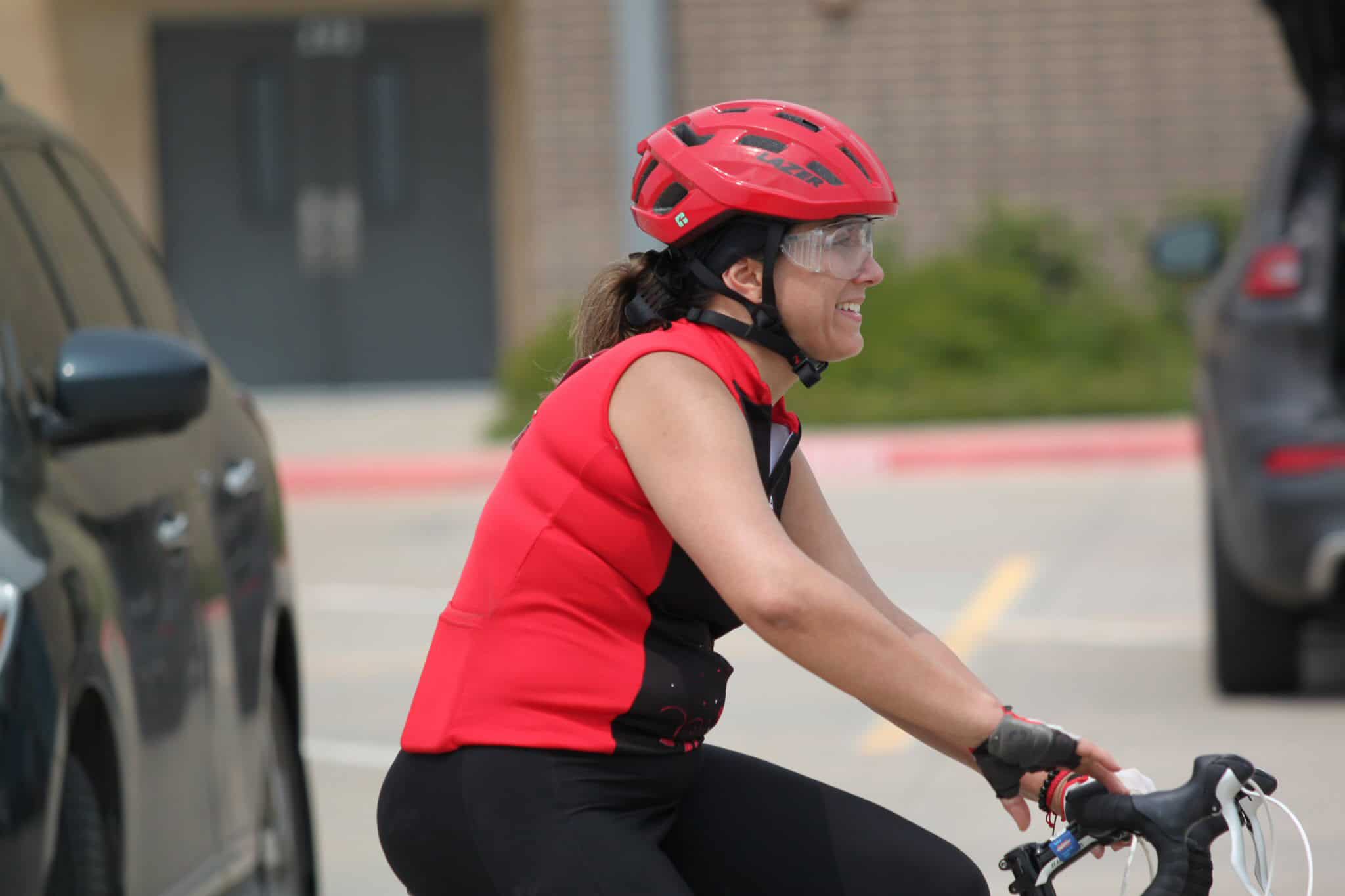 Cyclist smiling wearing a red helmet and vest on a mountain bike in a parking lot.