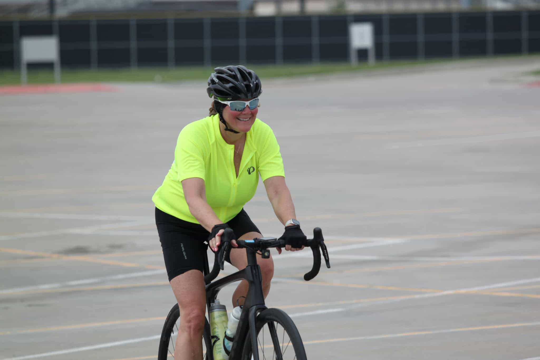 Bright yellow cycling jersey woman riding a bike in an open parking lot.