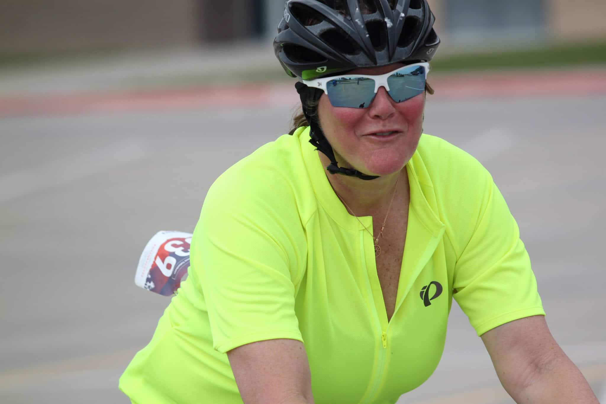 Vibrant woman cyclist in neon yellow jersey, sunglasses, and helmet enjoying ride on Bluebonnet Express route.
