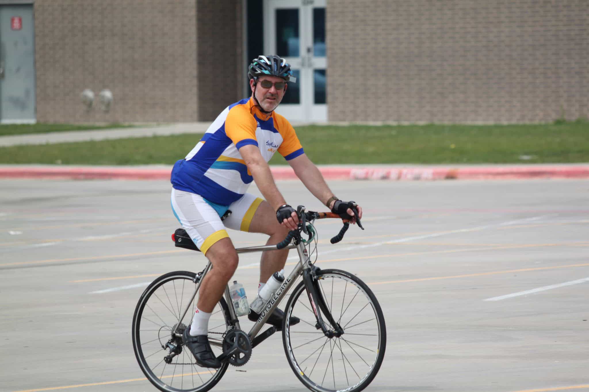Brightly colored cyclist riding on bike in open parking lot with school building background.