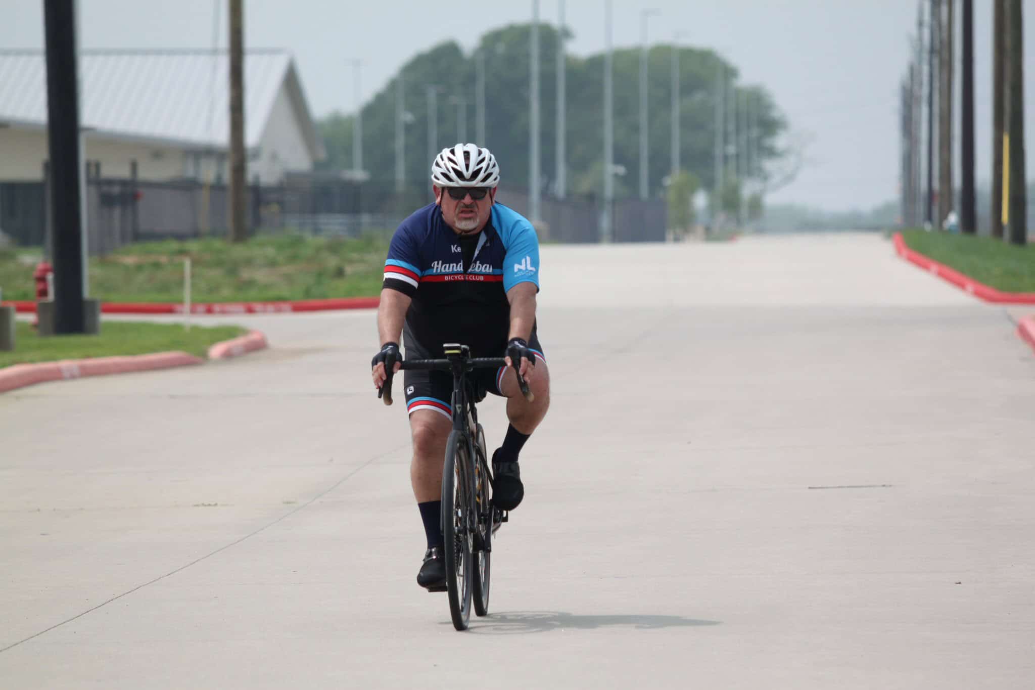Older man cycling on a road wearing a blue, black, and red cycling jersey with a helmet.