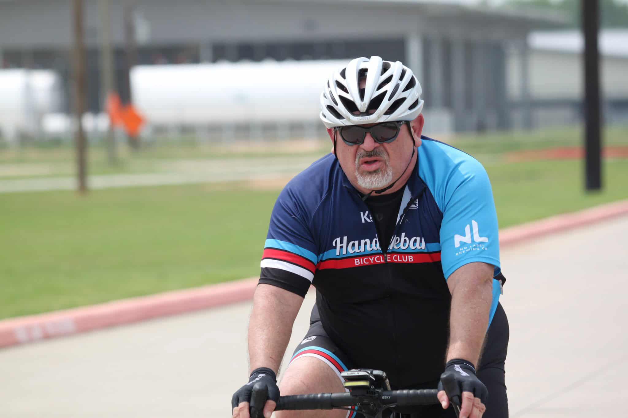 Cyclist wearing Bluebonnet Express cycling jersey with helmet and sunglasses on outdoor road.