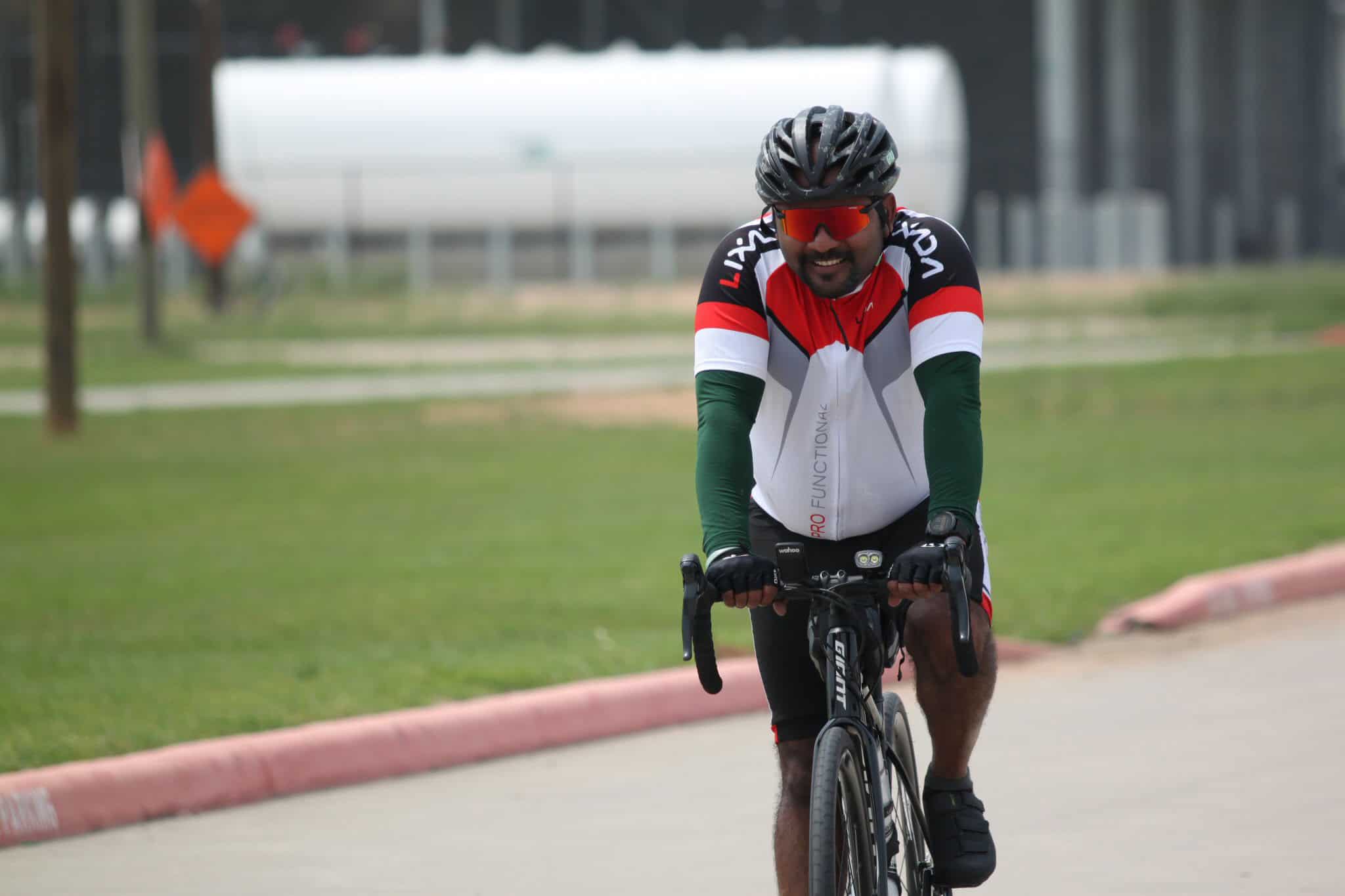 Bright cyclist wearing Red and Green jersey, riding a bike outdoors on a paved trail.
