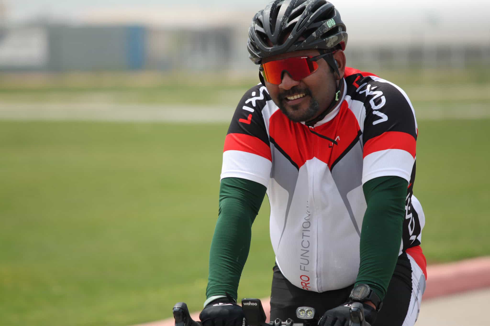 Comfortable cyclist wearing helmet and sunglasses on a ride in open green space.