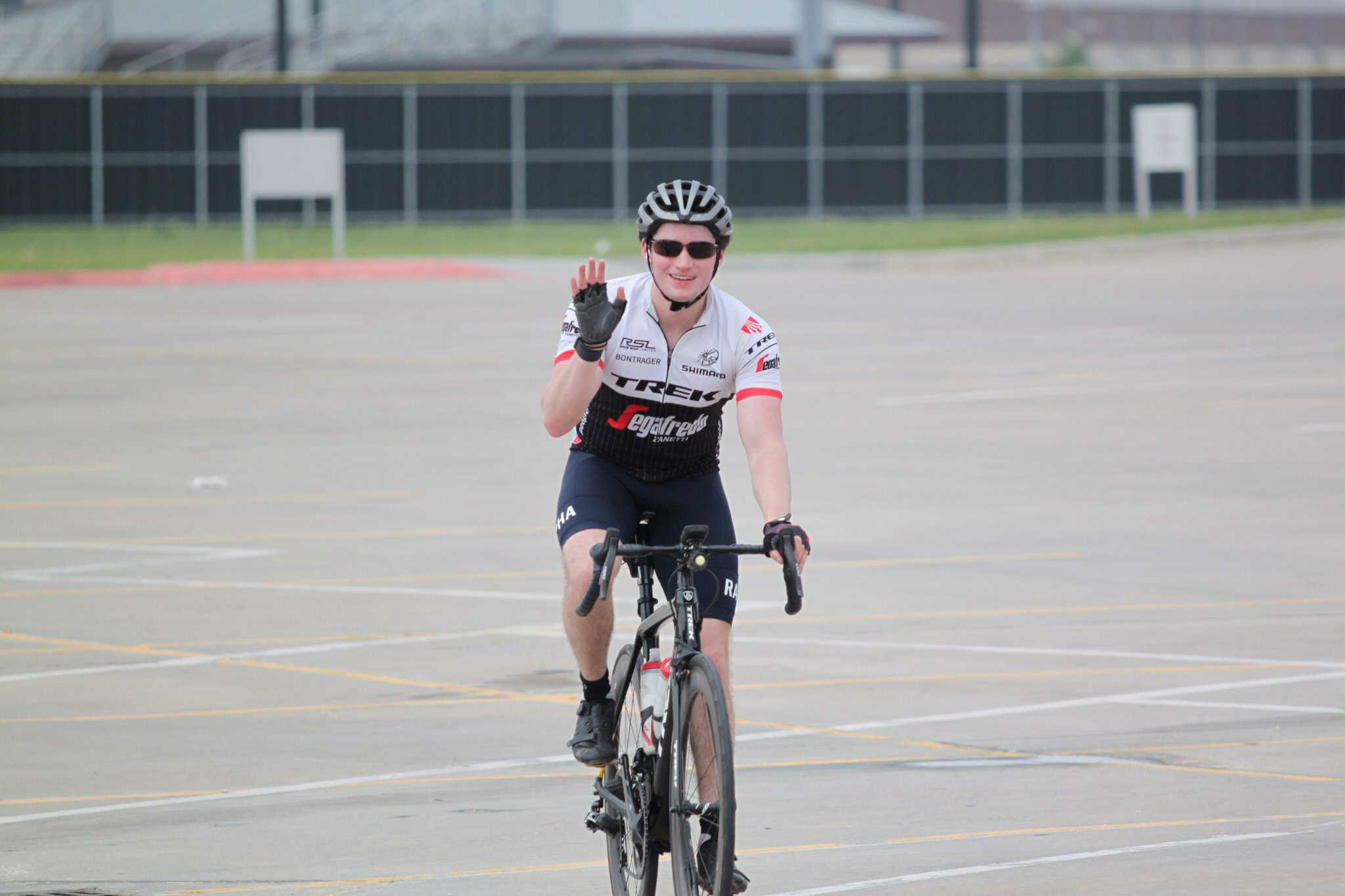Vibrant cyclist waving on empty parking lot road with Bluebonnet Express logo on jersey.
