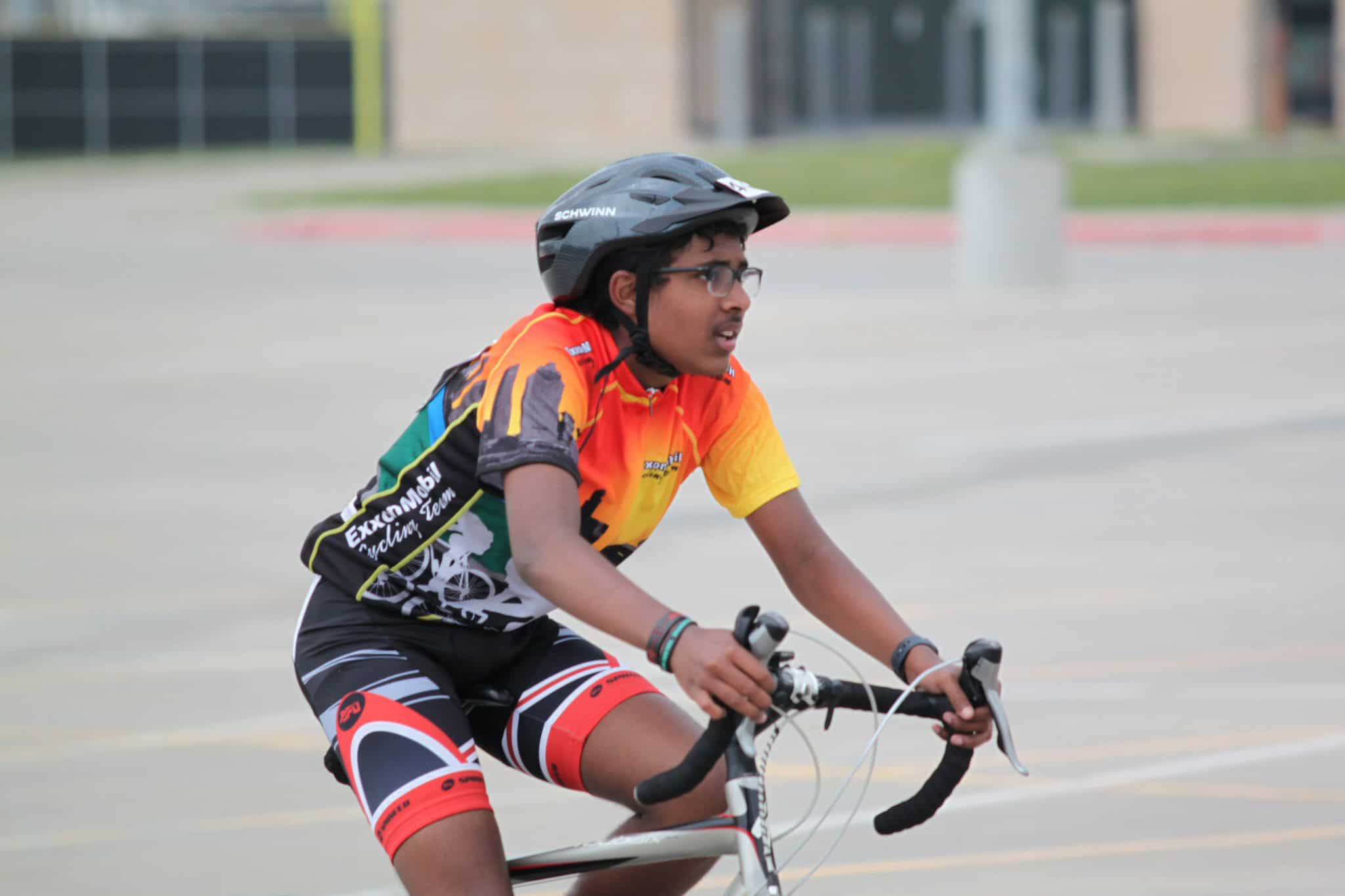 Young cyclist wearing a colorful Jersey and helmet riding during daytime.