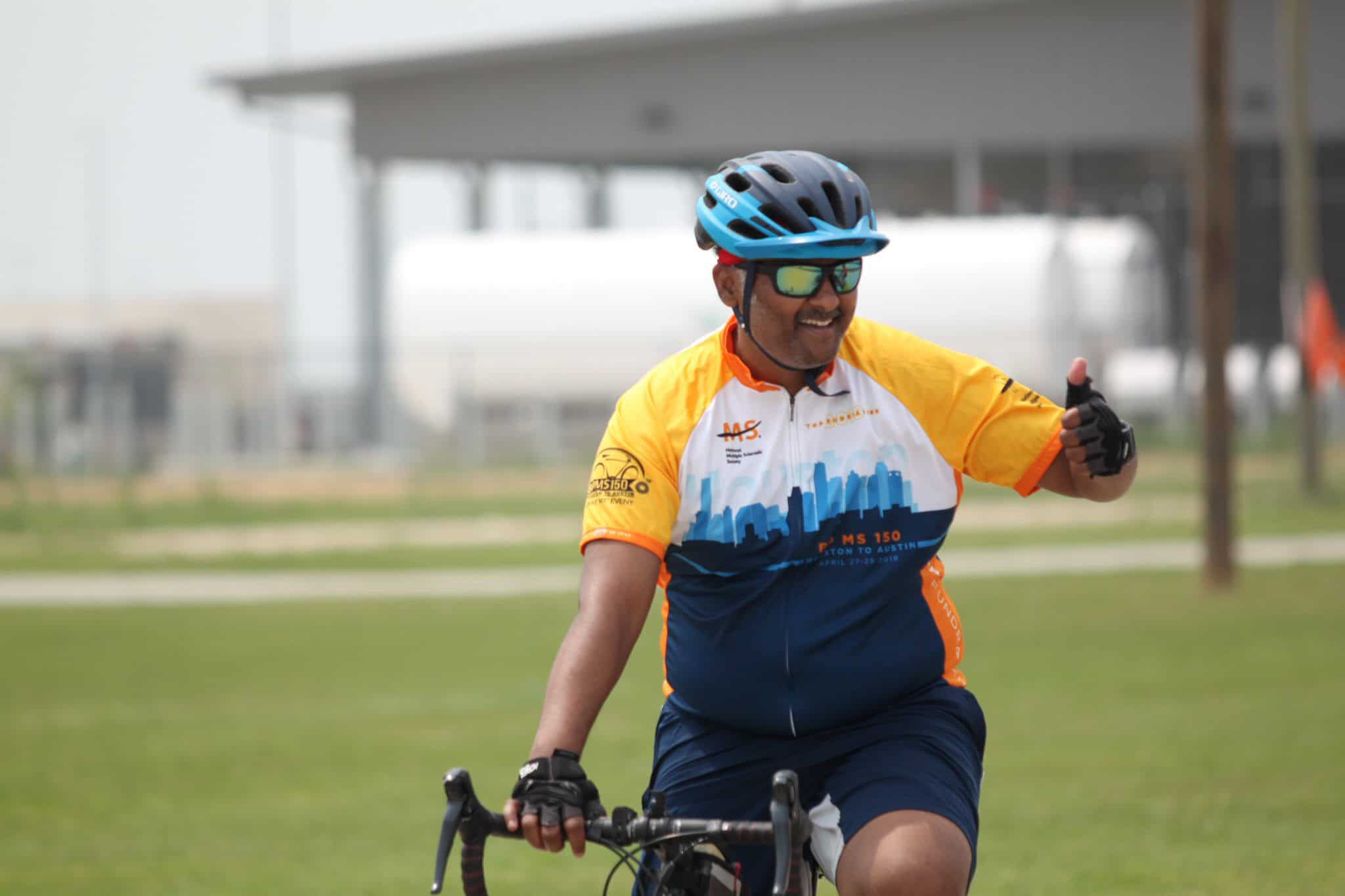 Smiling cyclist wearing a blue helmet and sunglasses riding during Bluebonnet Express event.