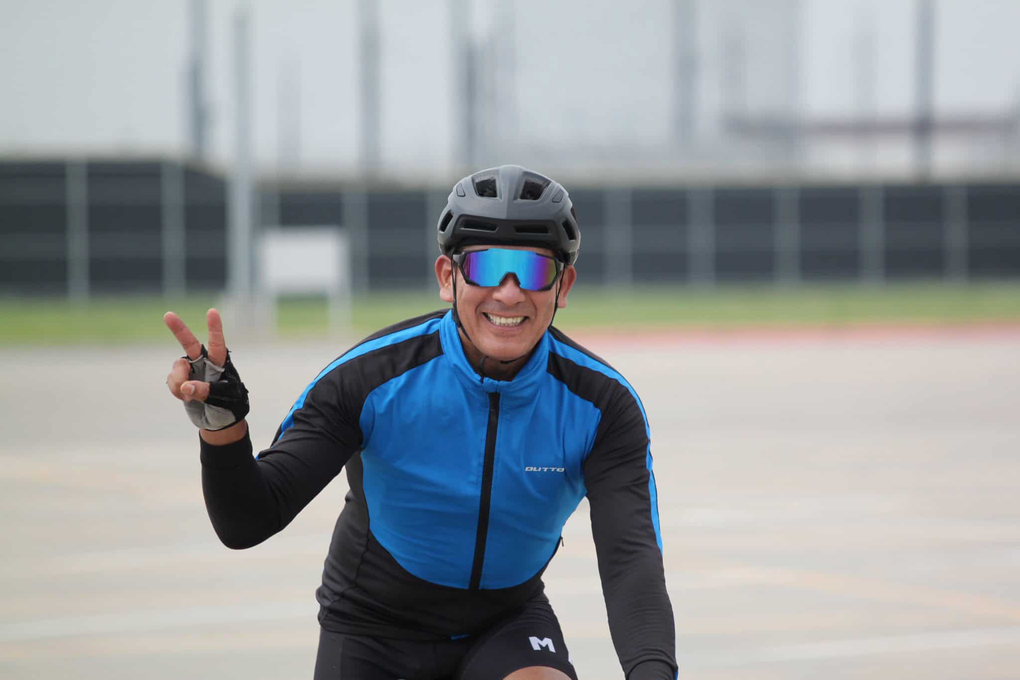 Vibrant cyclist in blue riding gear smiling with peace sign at outdoor track.