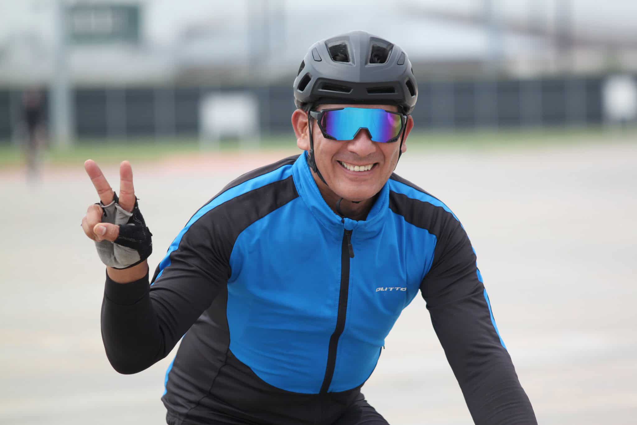 Vibrant cyclist wearing blue jersey and helmet, flashing peace sign at Bluebonnet Express event.