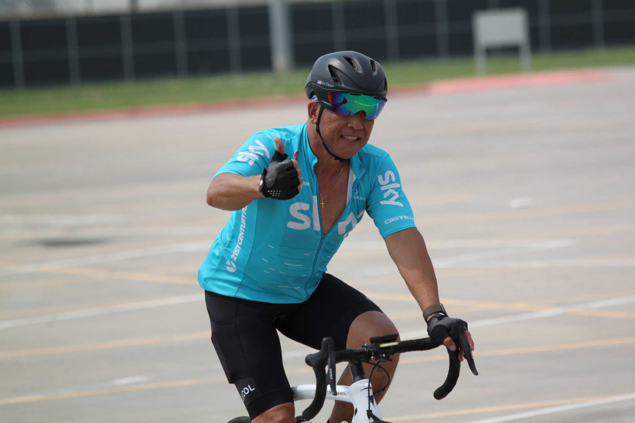 Optimized ALT: Cyclist in Bluebonnet Express cycling jersey with helmet and sunglasses giving thumbs up.