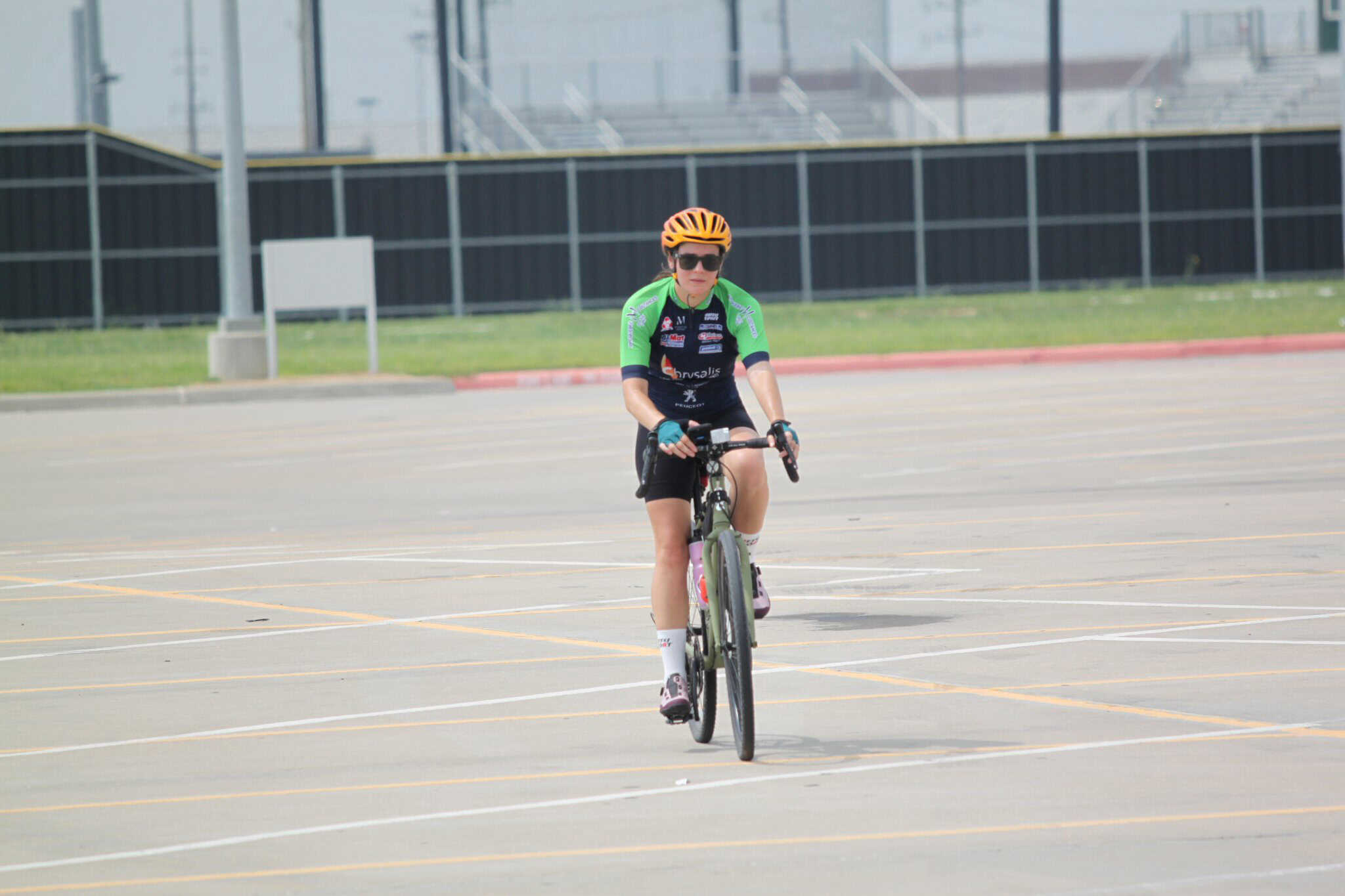 Bright green and black cycling jersey, orange helmet, and sunglasses on cyclist riding in empty parking lot for Bluebonnet Express event.