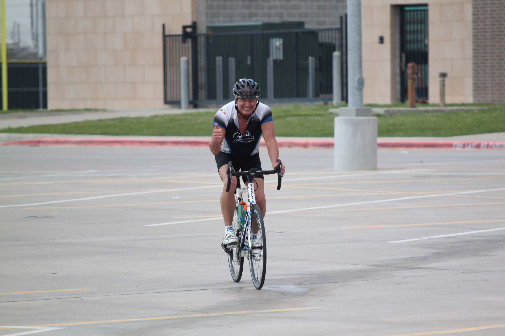 Smiling man riding a blue bicycle in an empty parking lot, celebrating success after a ride.