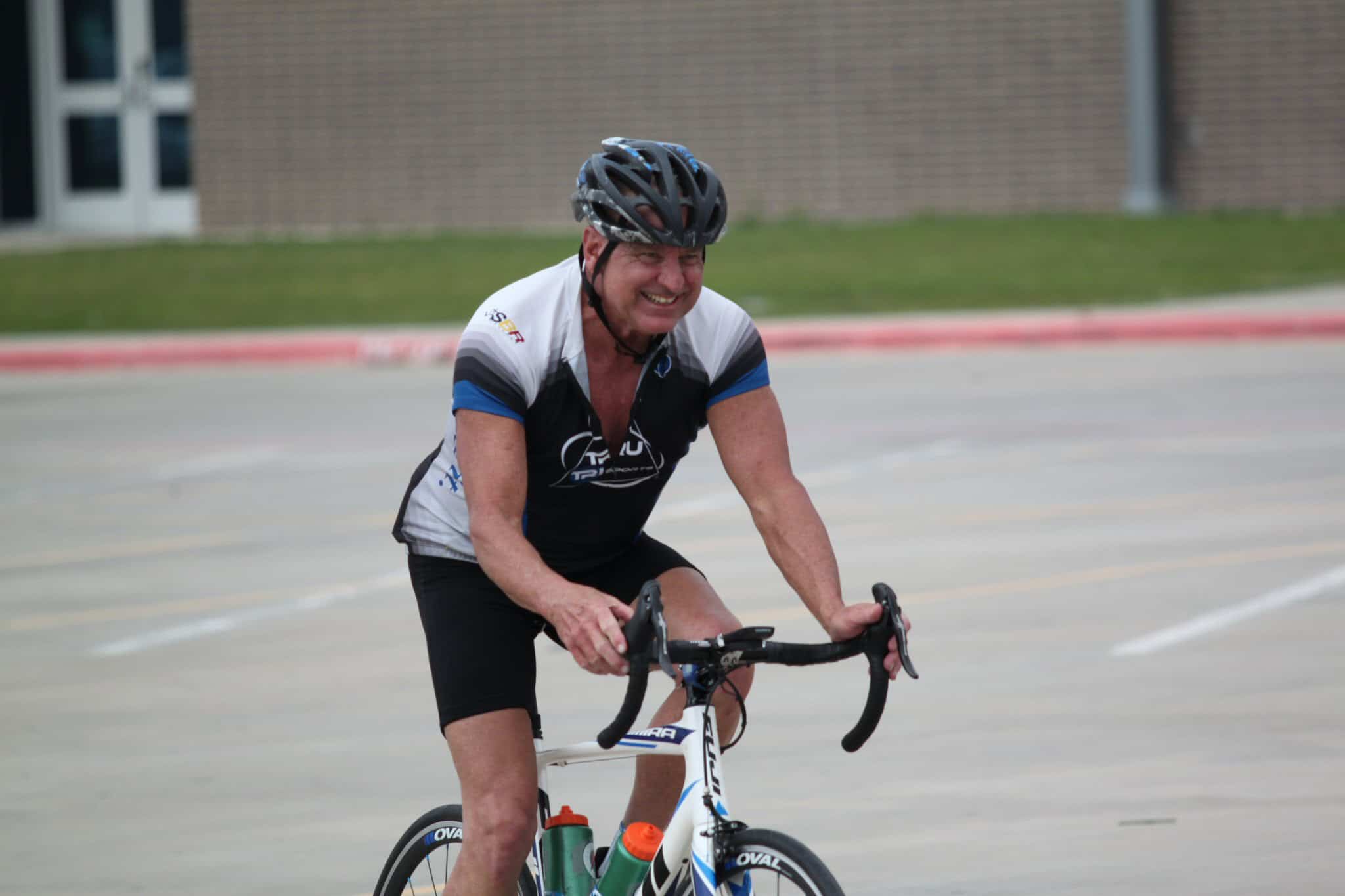 Happy man cycling outdoors on a road bike, wearing a helmet and sports attire.