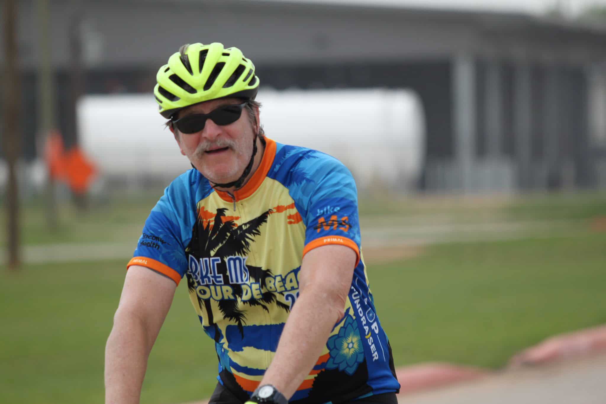 Vibrant cyclist wearing Bluebonnet Express cycling jersey, bike helmet, and sunglasses outdoors.