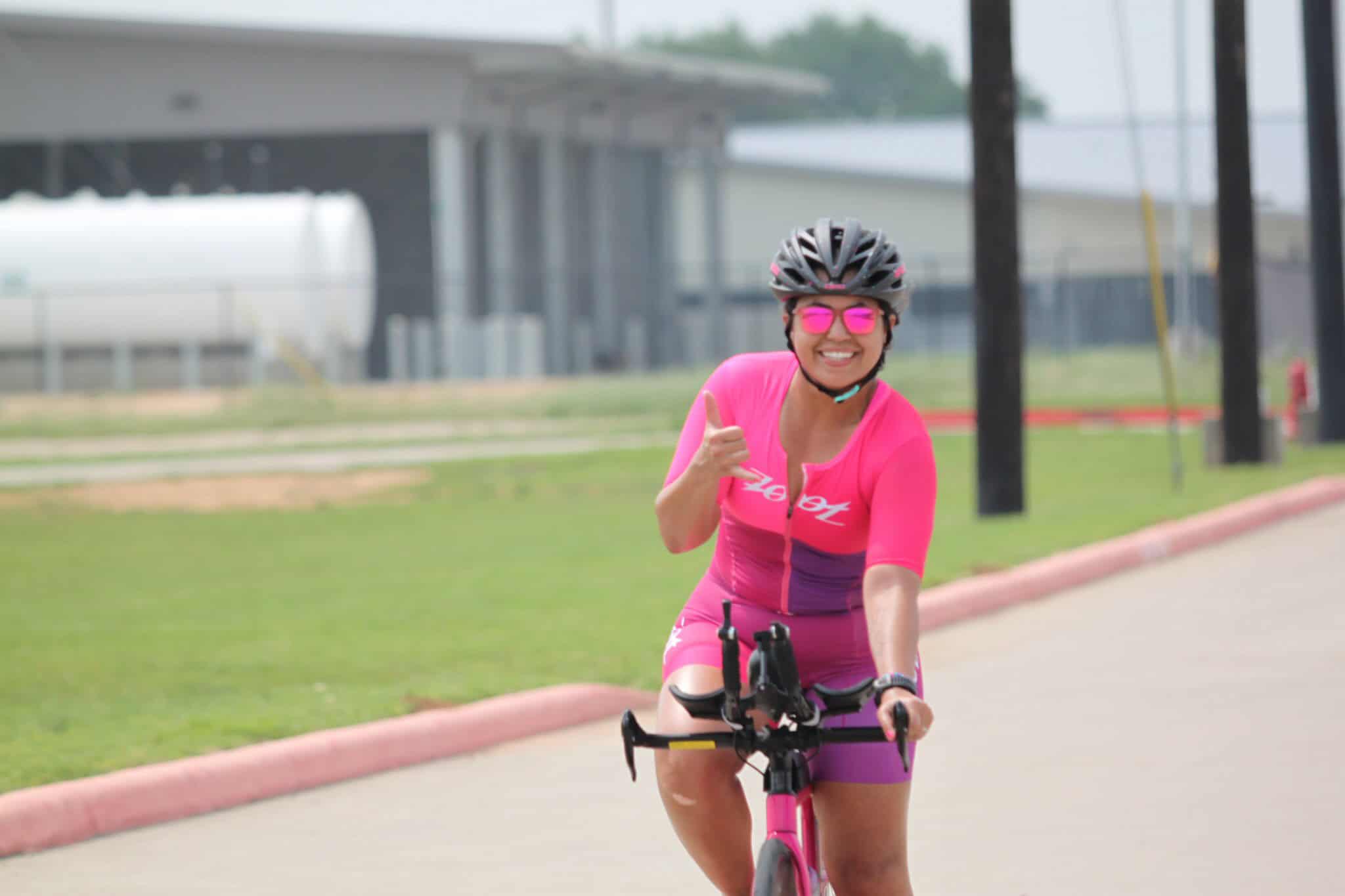 Bright pink cycling outfit, smiling woman riding bike on outdoor trail in vibrant gear.