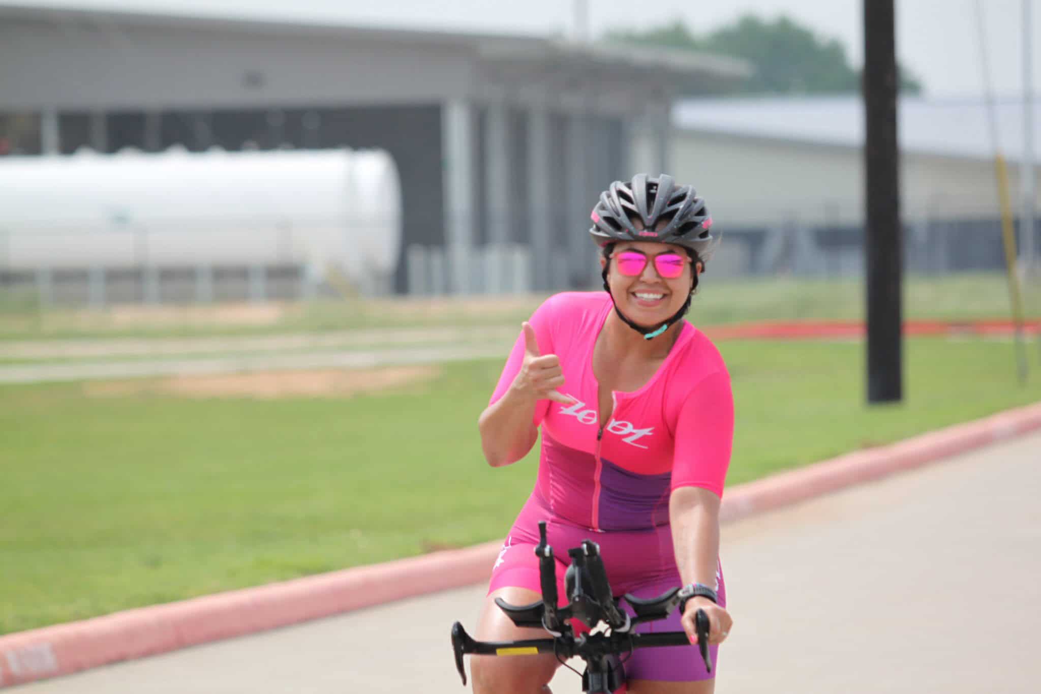 Bright pink cycling jersey and sunglasses, smiling woman enjoying bike ride, healthy outdoor activity, supporting Bluebonnet Express.