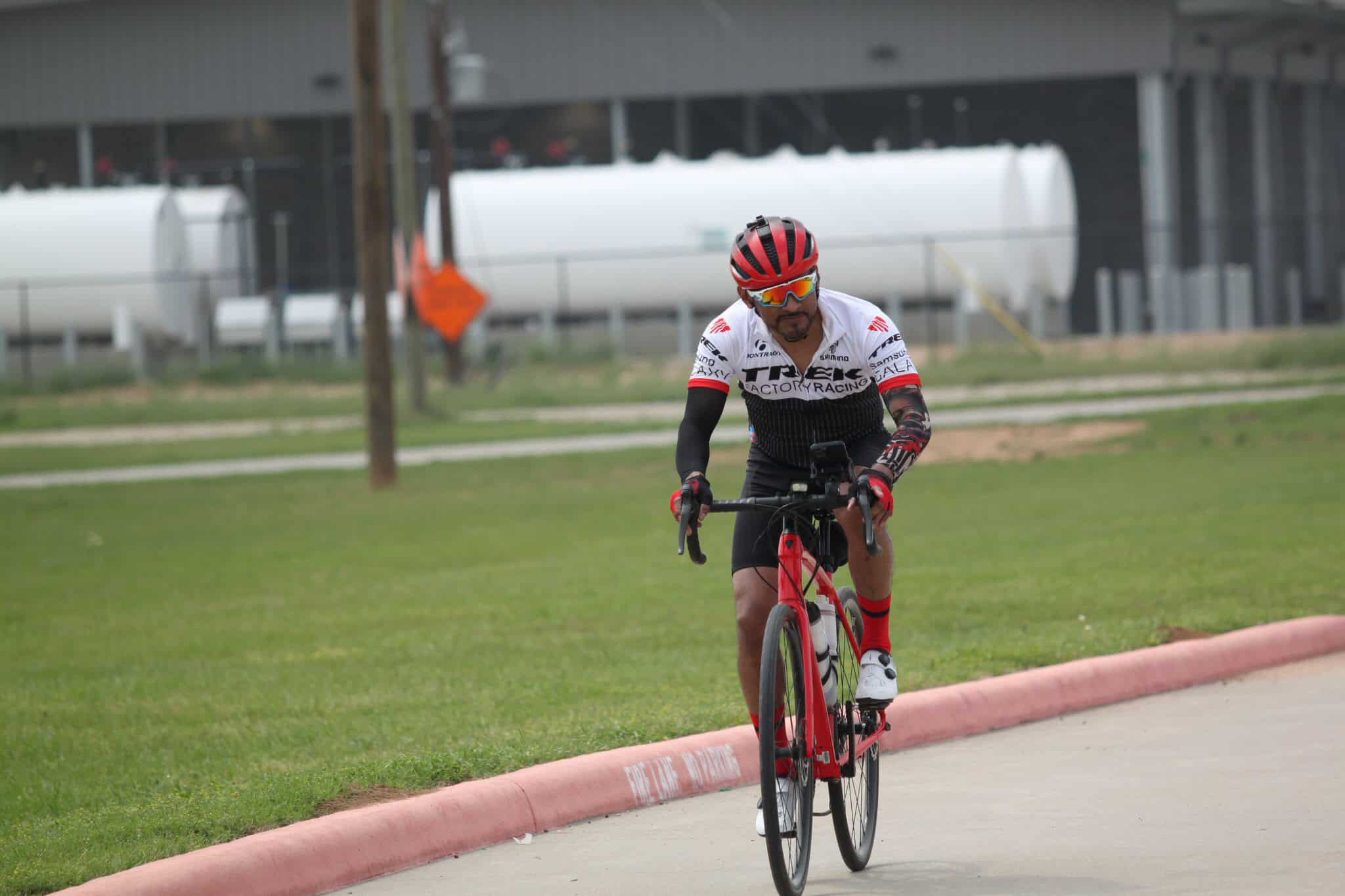 Man riding a red bicycle in cycling gear on a paved trail during daytime.