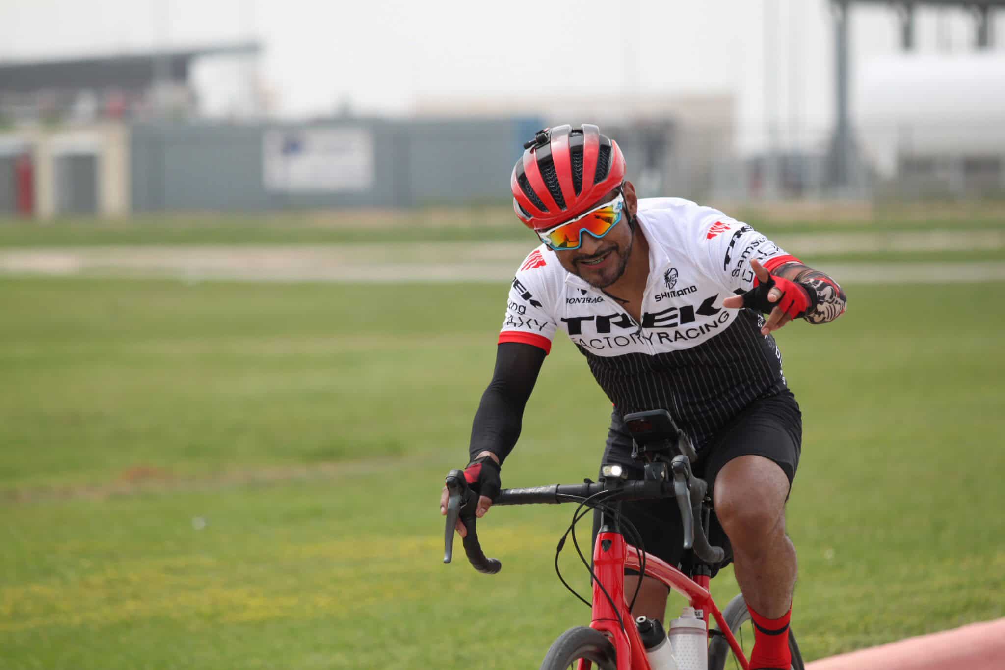 Bright red helmet and sunglasses on smiling cyclist riding a bike outdoors on a green field.